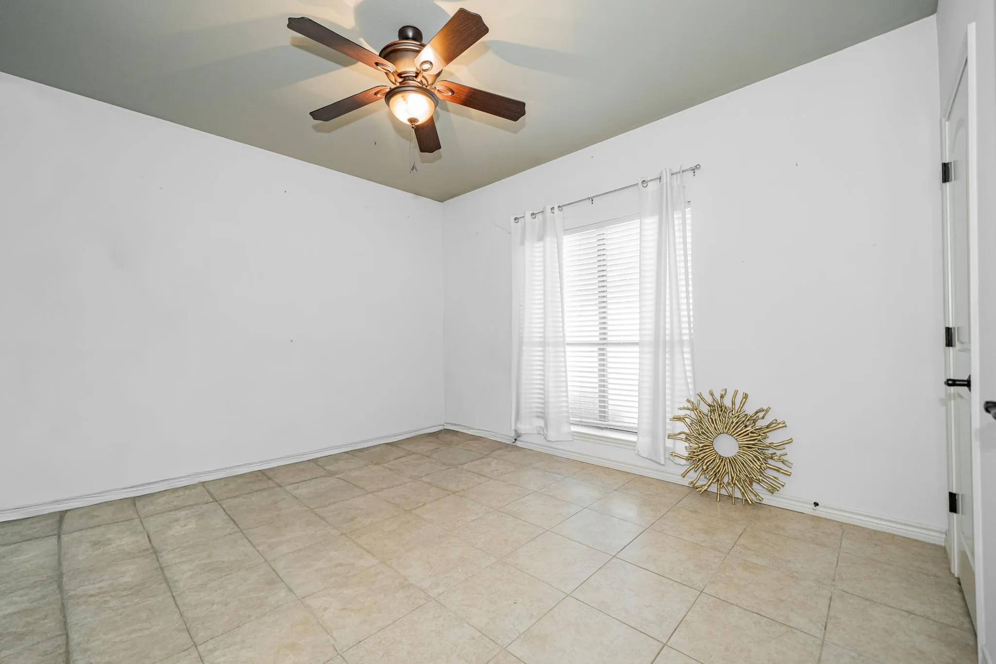 Room featuring tiled flooring, a ceiling fan with integrated lighting, and a single window with blinds and white curtains