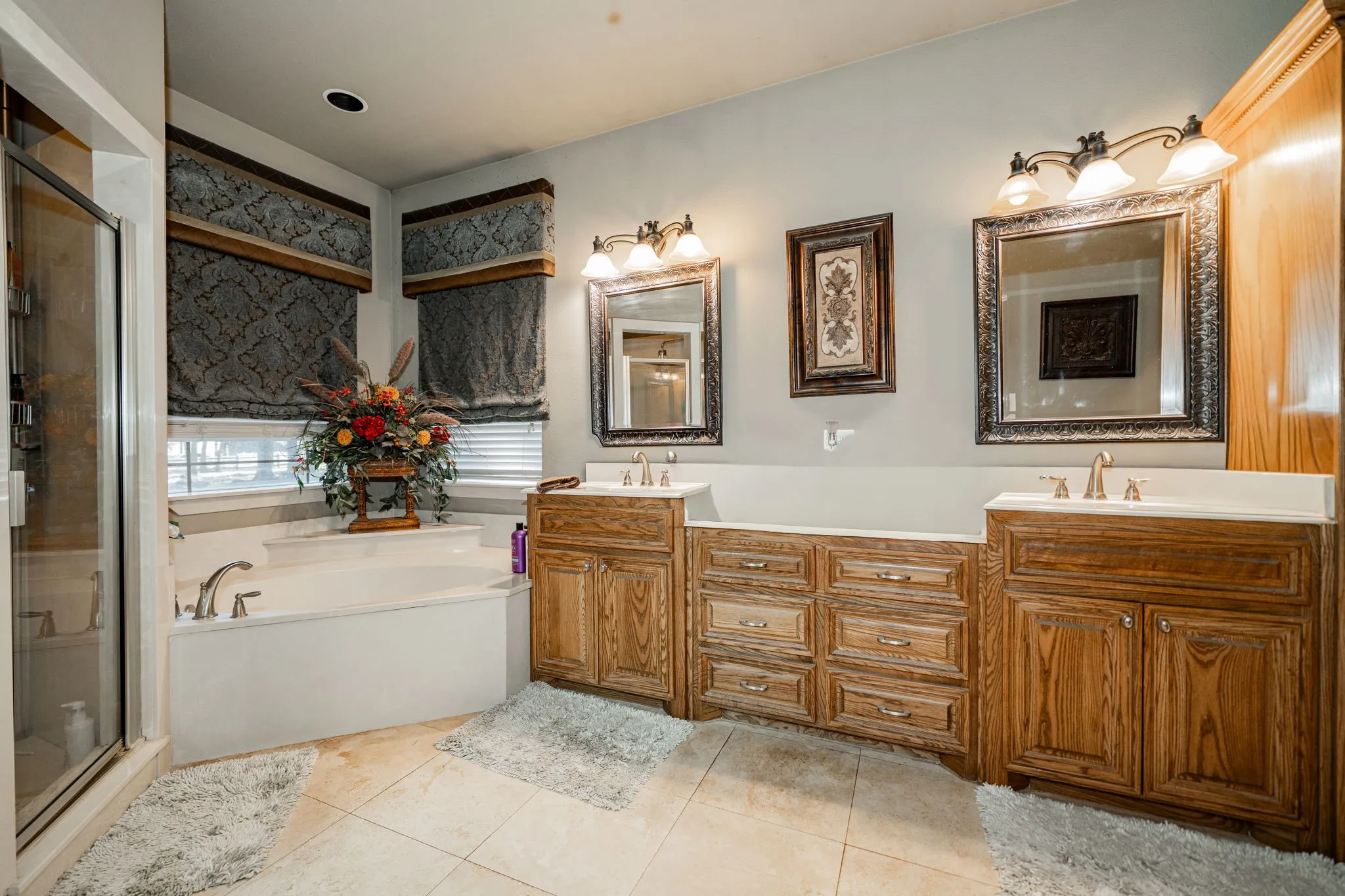 Bathroom featuring dual wood-finish vanities with light countertops, individual mirrors, and vanity lighting