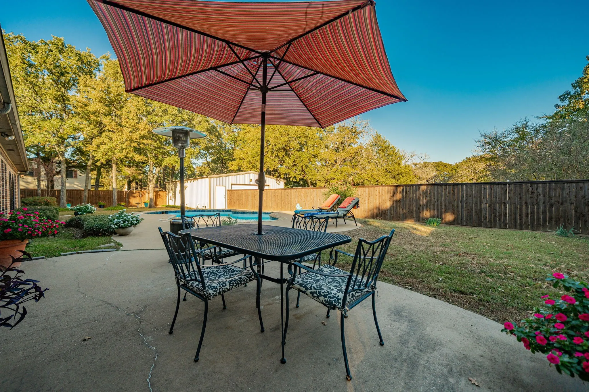 Expansive concrete patio offering ample outdoor living space, featuring a private swimming pool, a spacious grassy lawn, and a perimeter wood fence