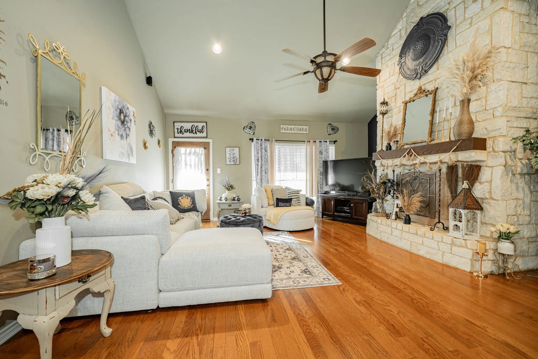 Spacious living area featuring a stone fireplace with a wood mantel, vaulted ceiling, wood-finish flooring, and a ceiling fan