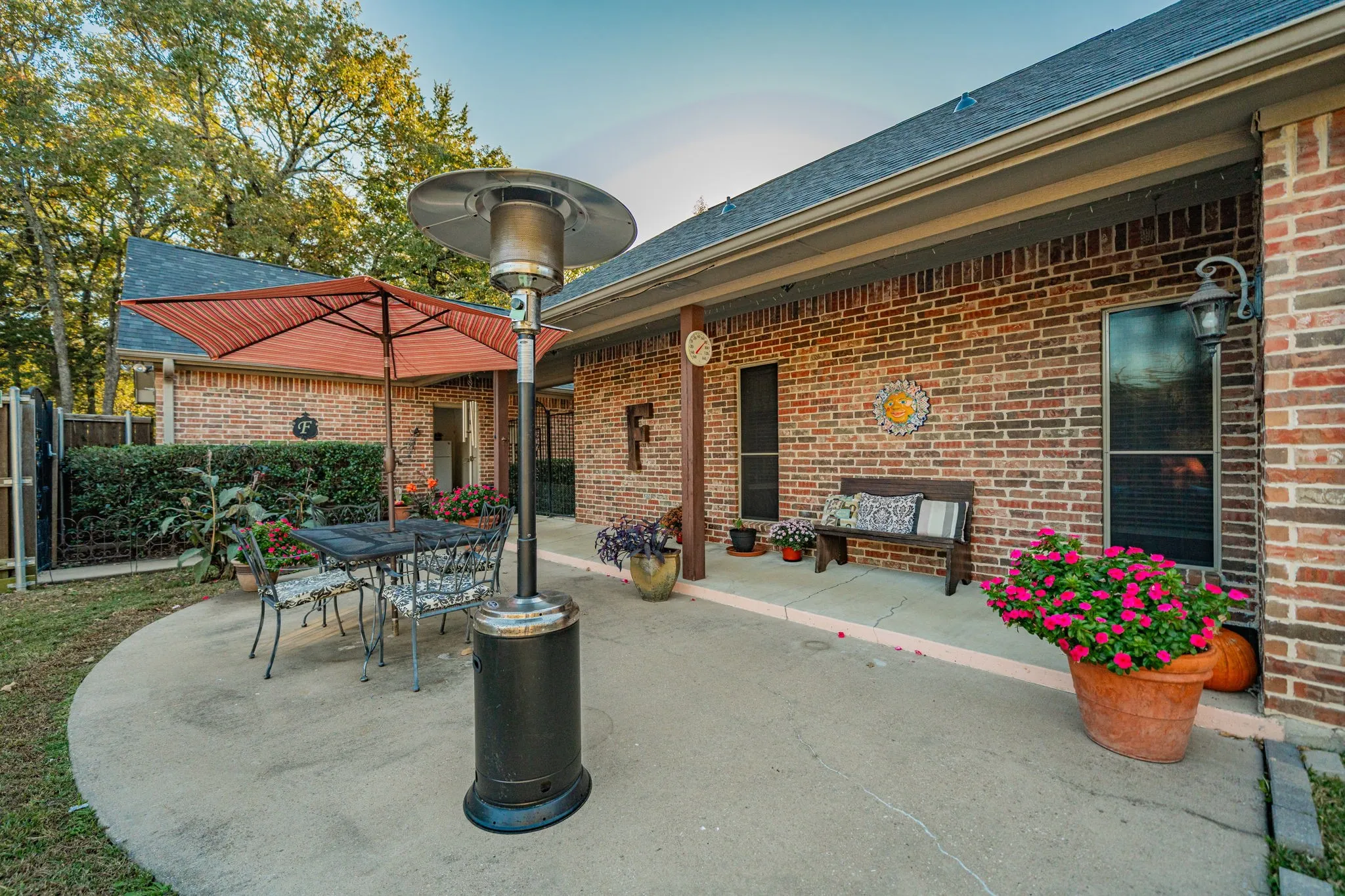 Expansive concrete patio with a brick exterior, covered porch area, and mature perimeter landscaping