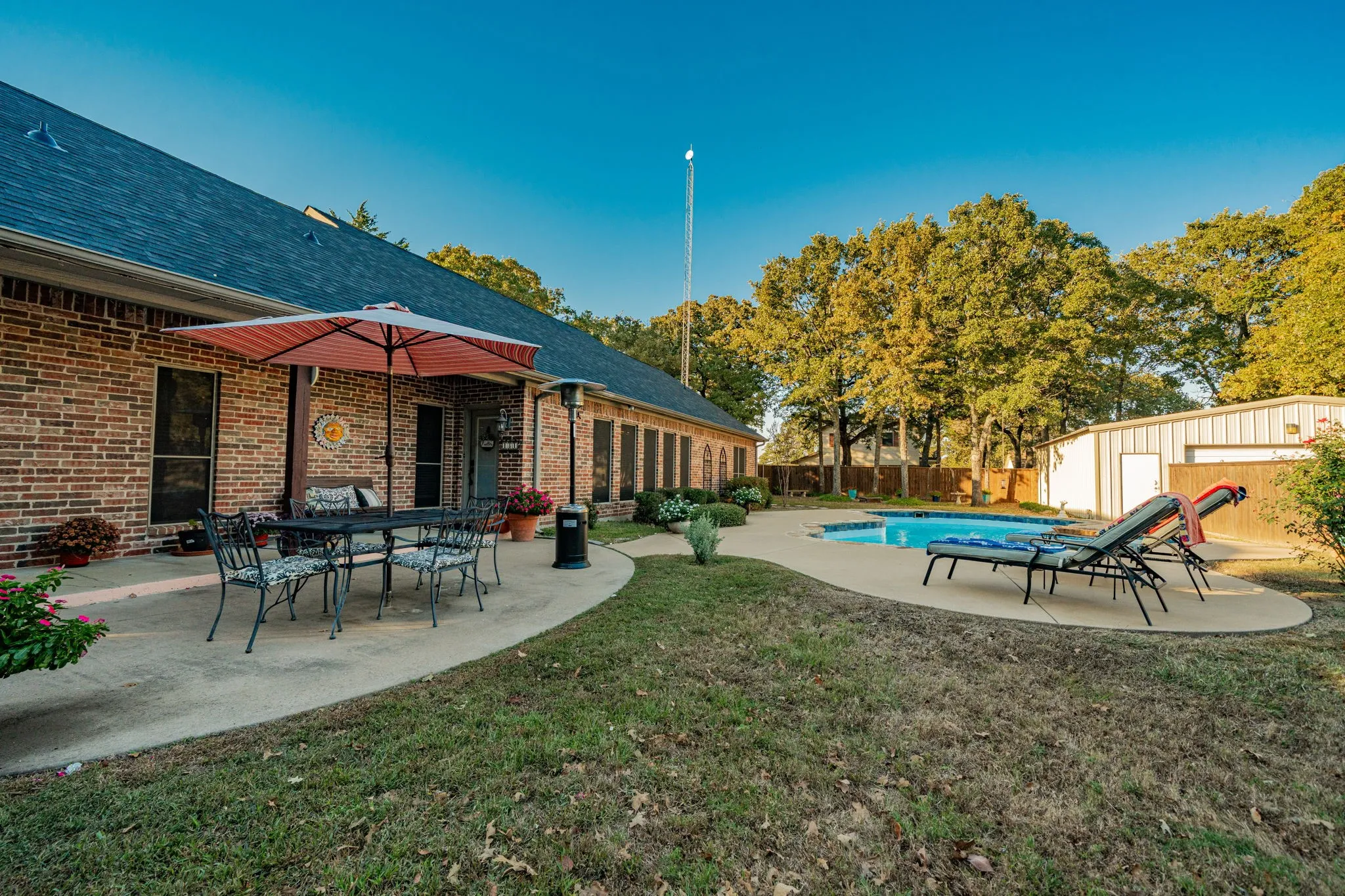 Expansive backyard featuring a curved concrete patio, a built-in swimming pool, mature trees, and a detached metal building