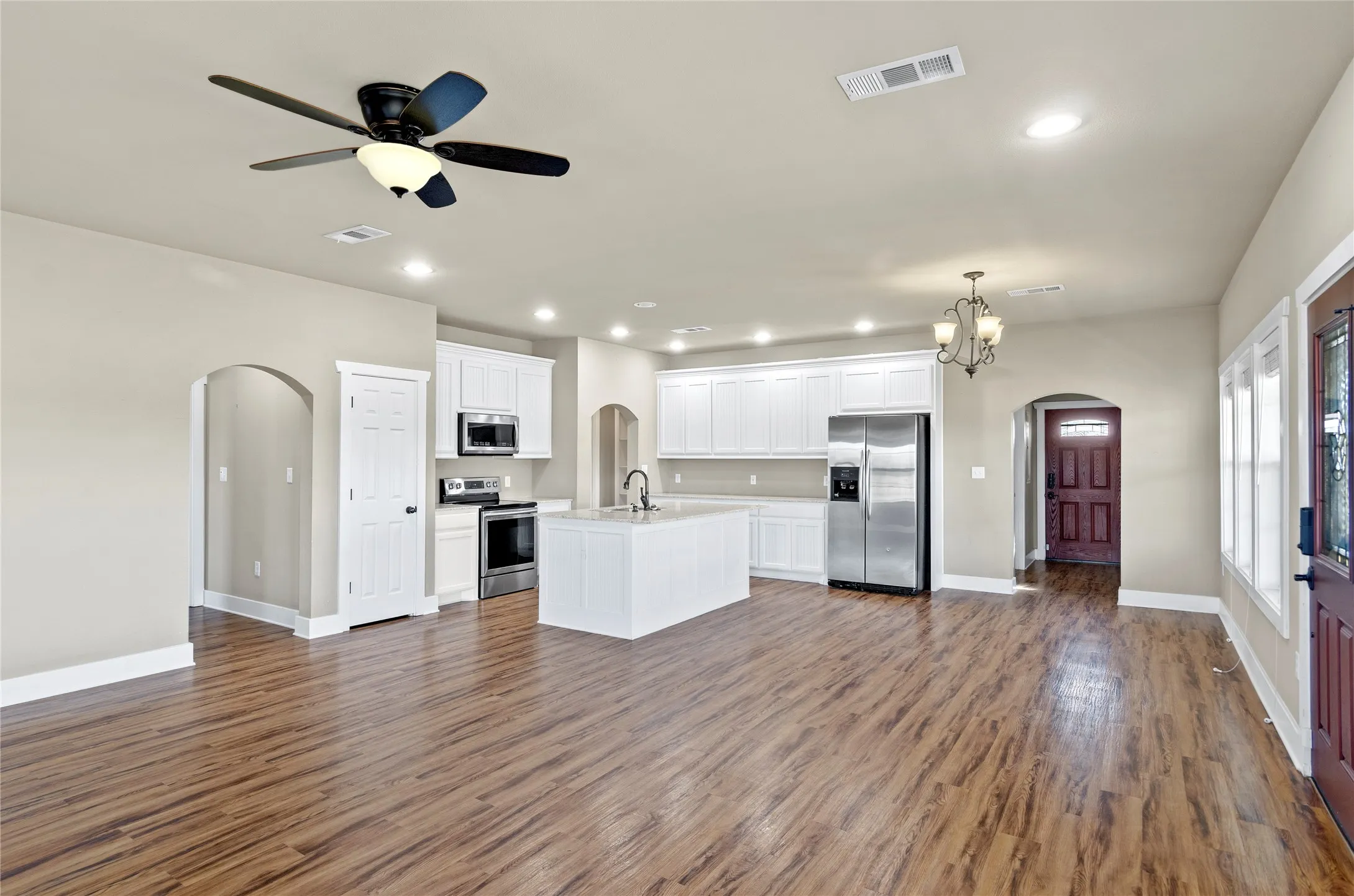 Kitchen featuring arched walkways, white cabinets, recessed lighting, stainless steel appliances, and open floor plan