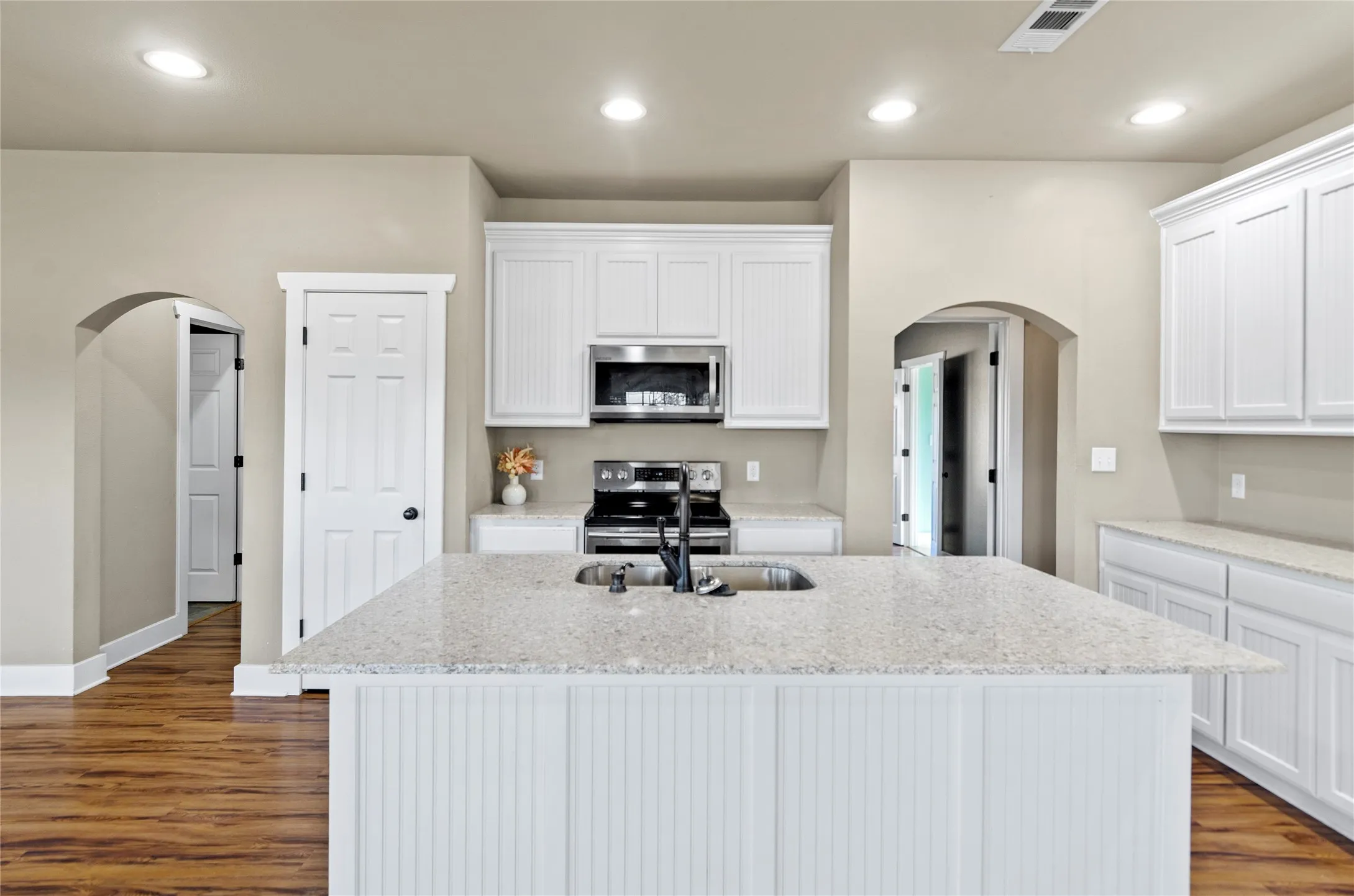Kitchen with arched walkways, white cabinets, light stone countertops, stainless steel appliances, and a center island with sink