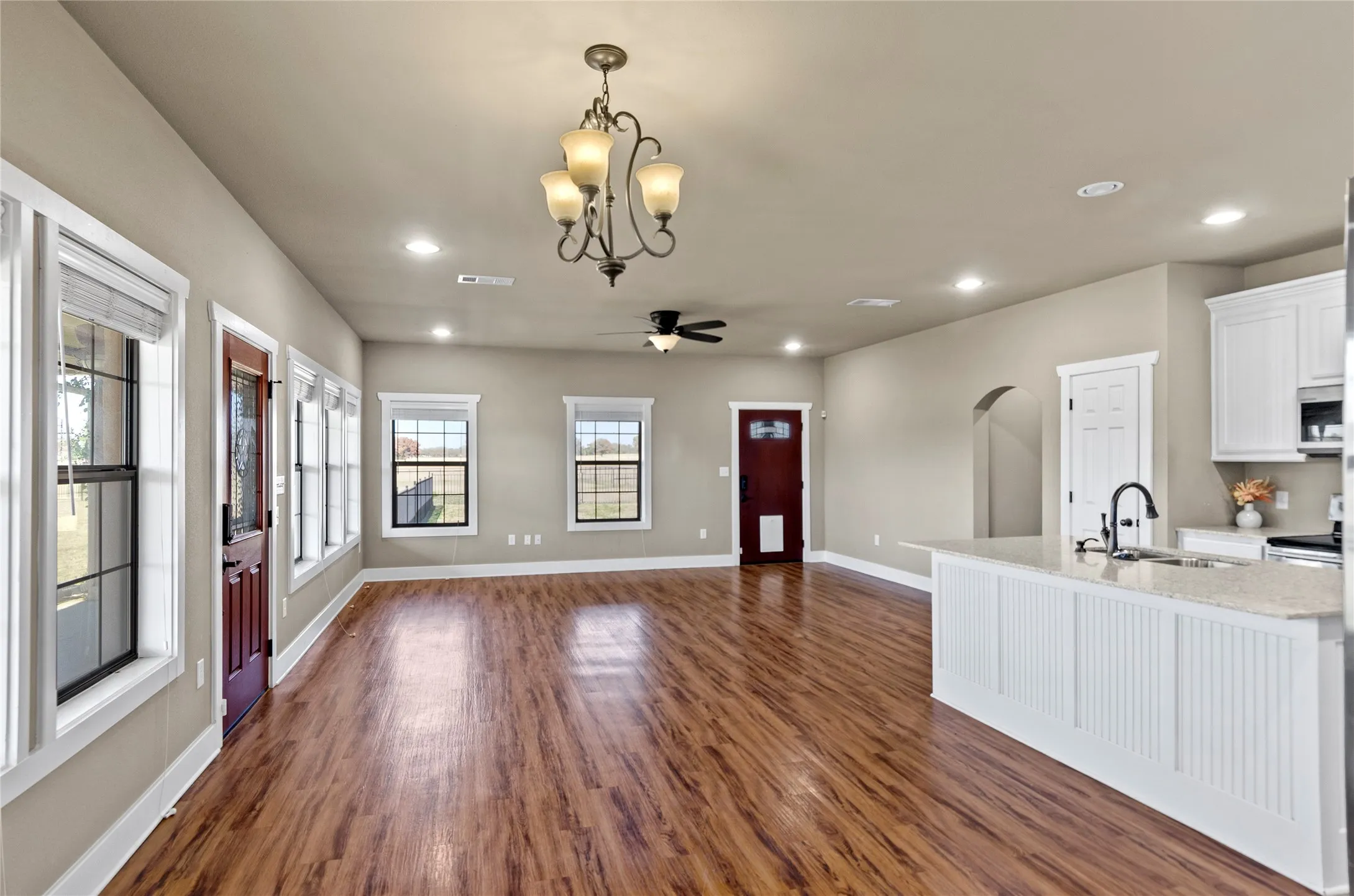 Kitchen with white cabinetry, arched walkways, decorative light fixtures, light stone counters, and recessed lighting