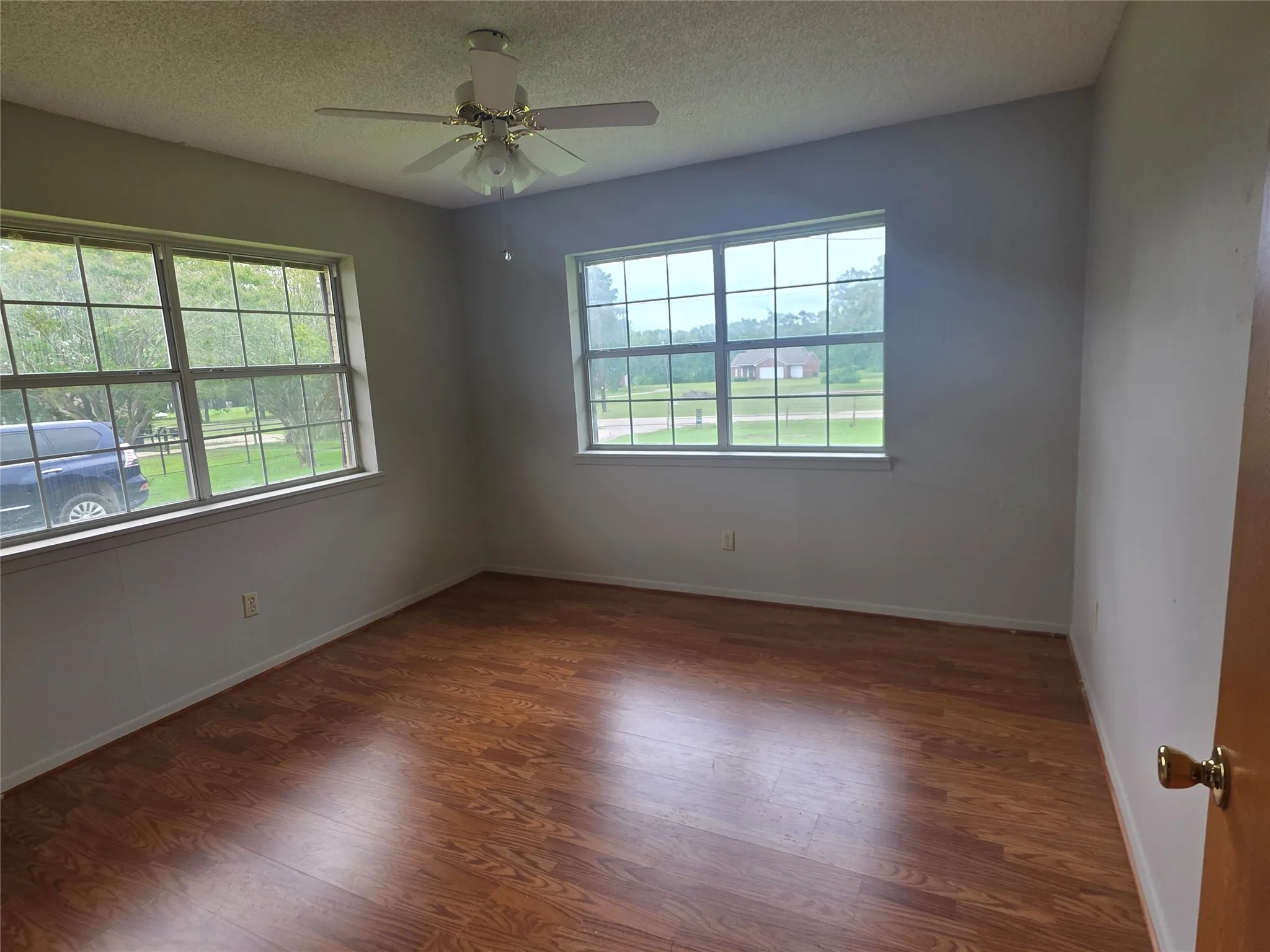 Room featuring two windows with white grilles, wood-finish flooring, and a ceiling fan with light fixture