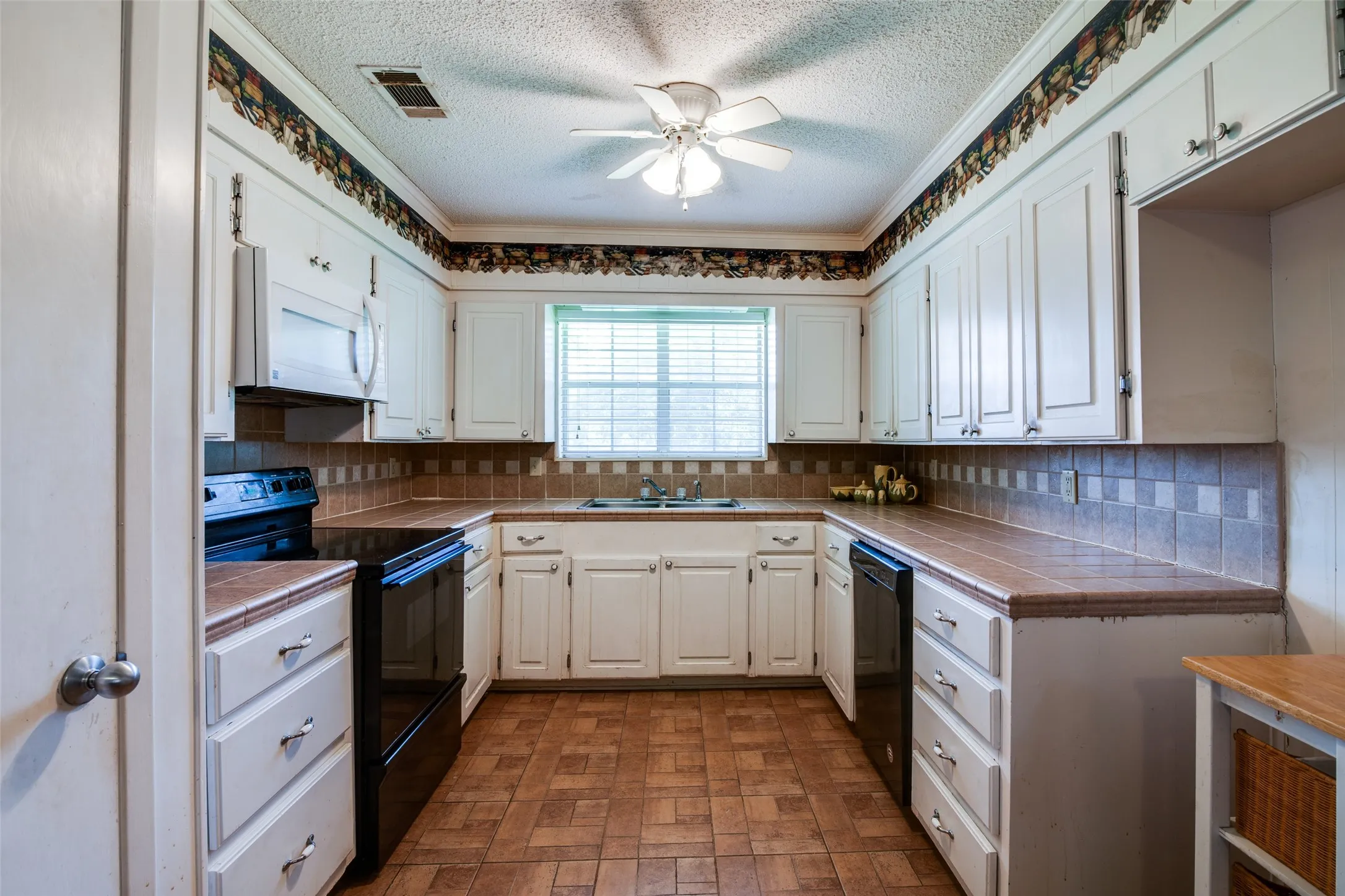 U-shaped kitchen featuring white cabinetry, tile countertops, tile backsplash, and a ceiling fan