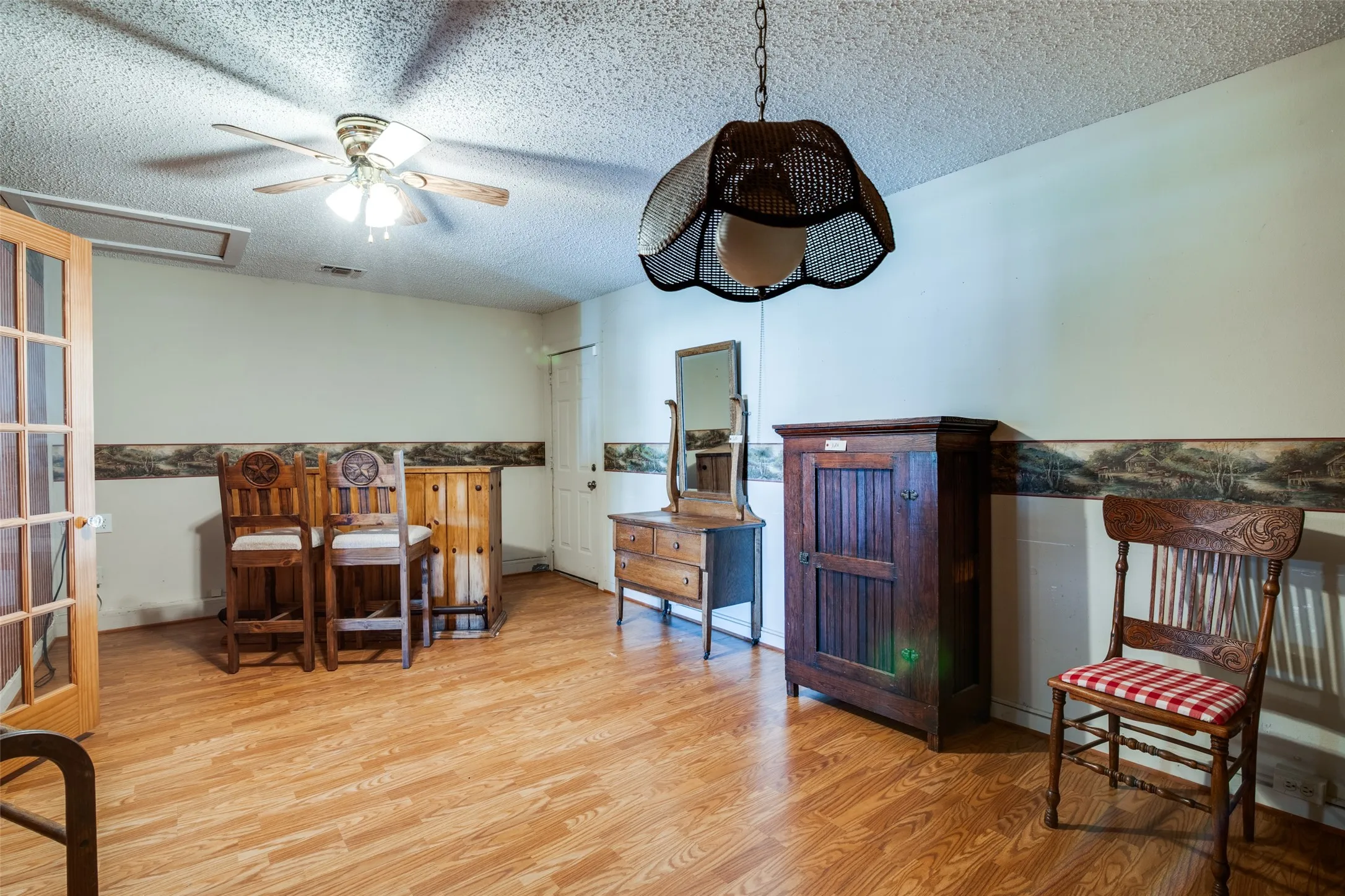 Wood-finish flooring throughout, featuring a ceiling fan with integrated lighting, a decorative pendant light fixture, and French doors with clear glass panels