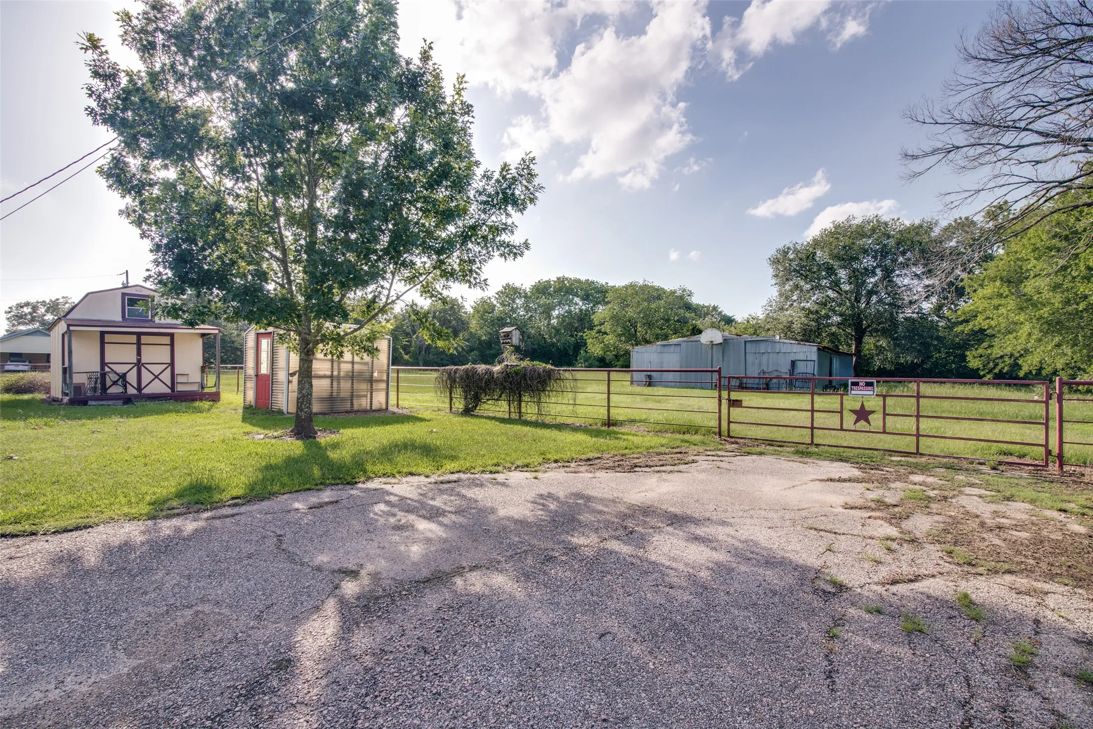 Expansive property featuring a metal security gate, gravel driveway, and a large metal outbuilding