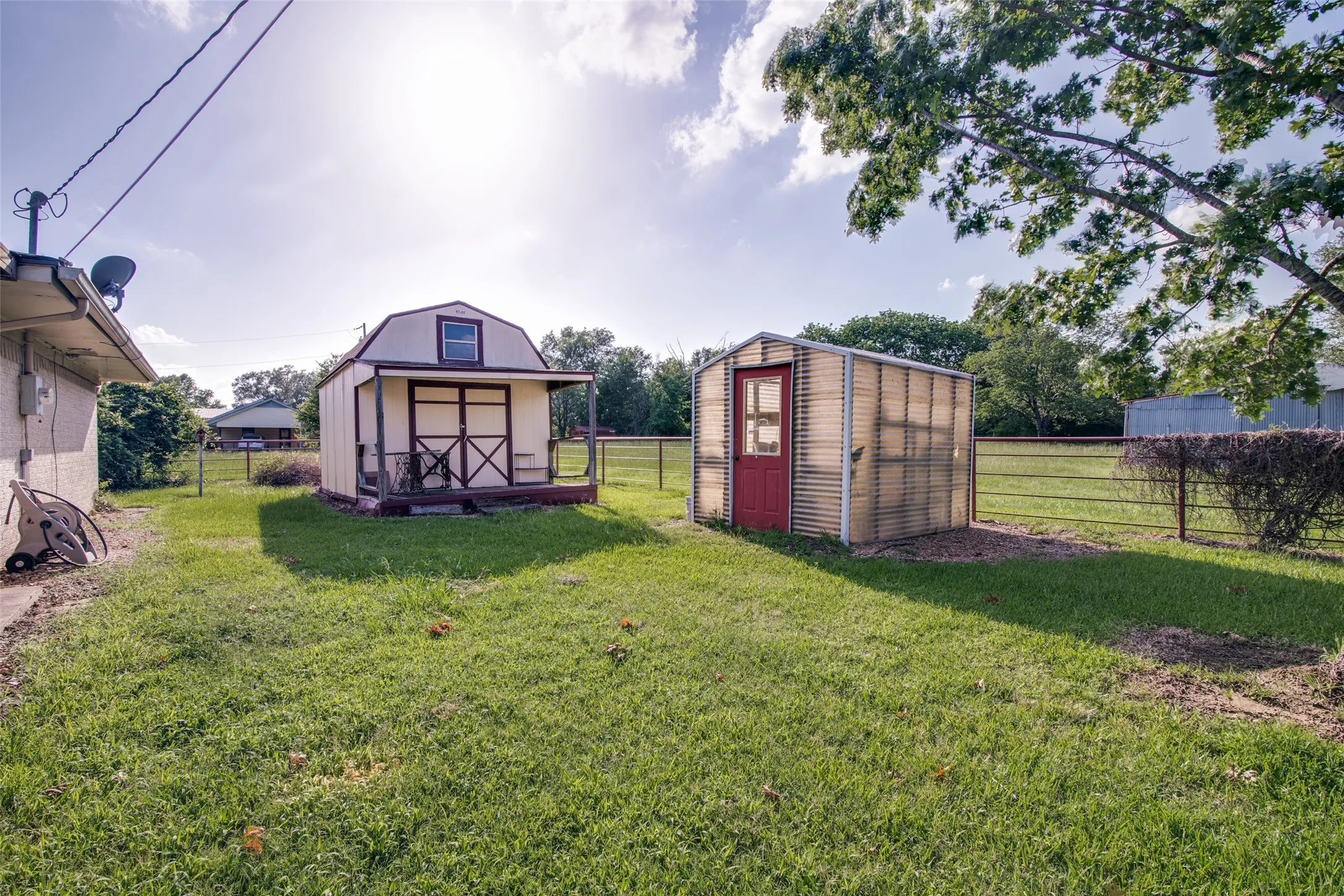 Expansive backyard featuring a gambrel-roofed outbuilding with porch, a translucent greenhouse with a red door, and a perimeter fence