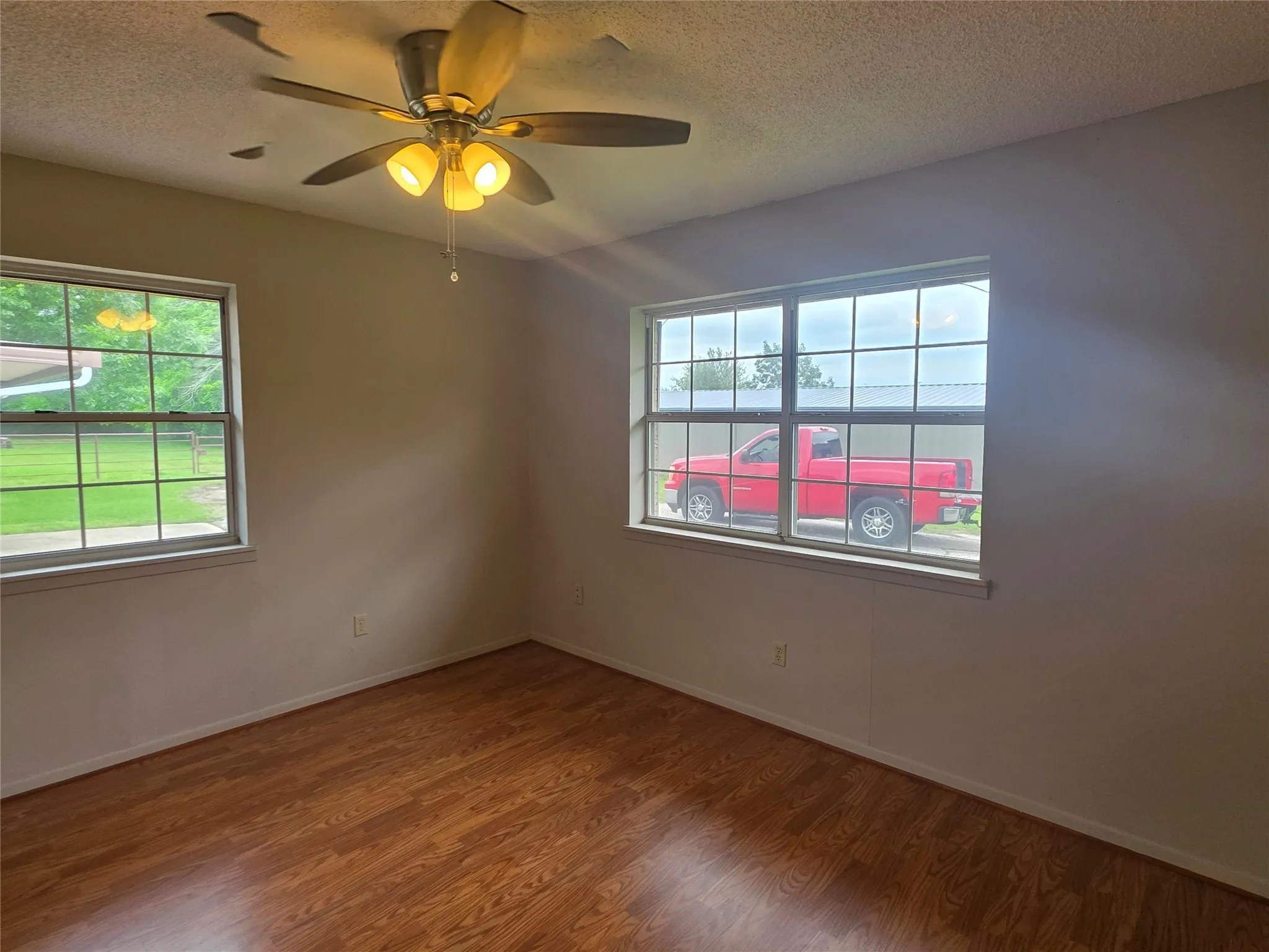 Interior space featuring wood-finish flooring, two window units, and a ceiling fan with integrated lighting