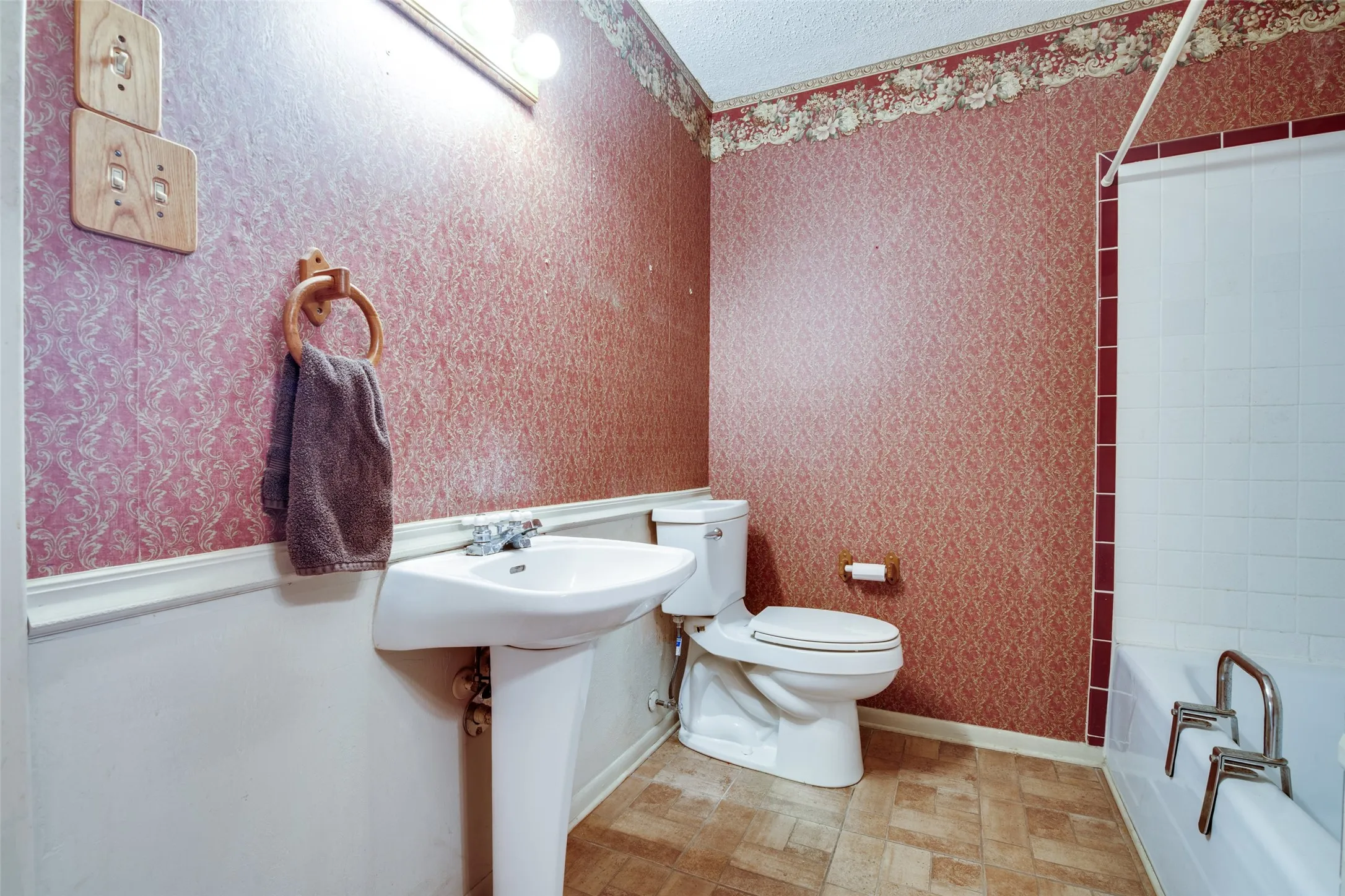Pedestal sink with chrome faucet, toilet, and bathtub with white tile surround featuring red trim