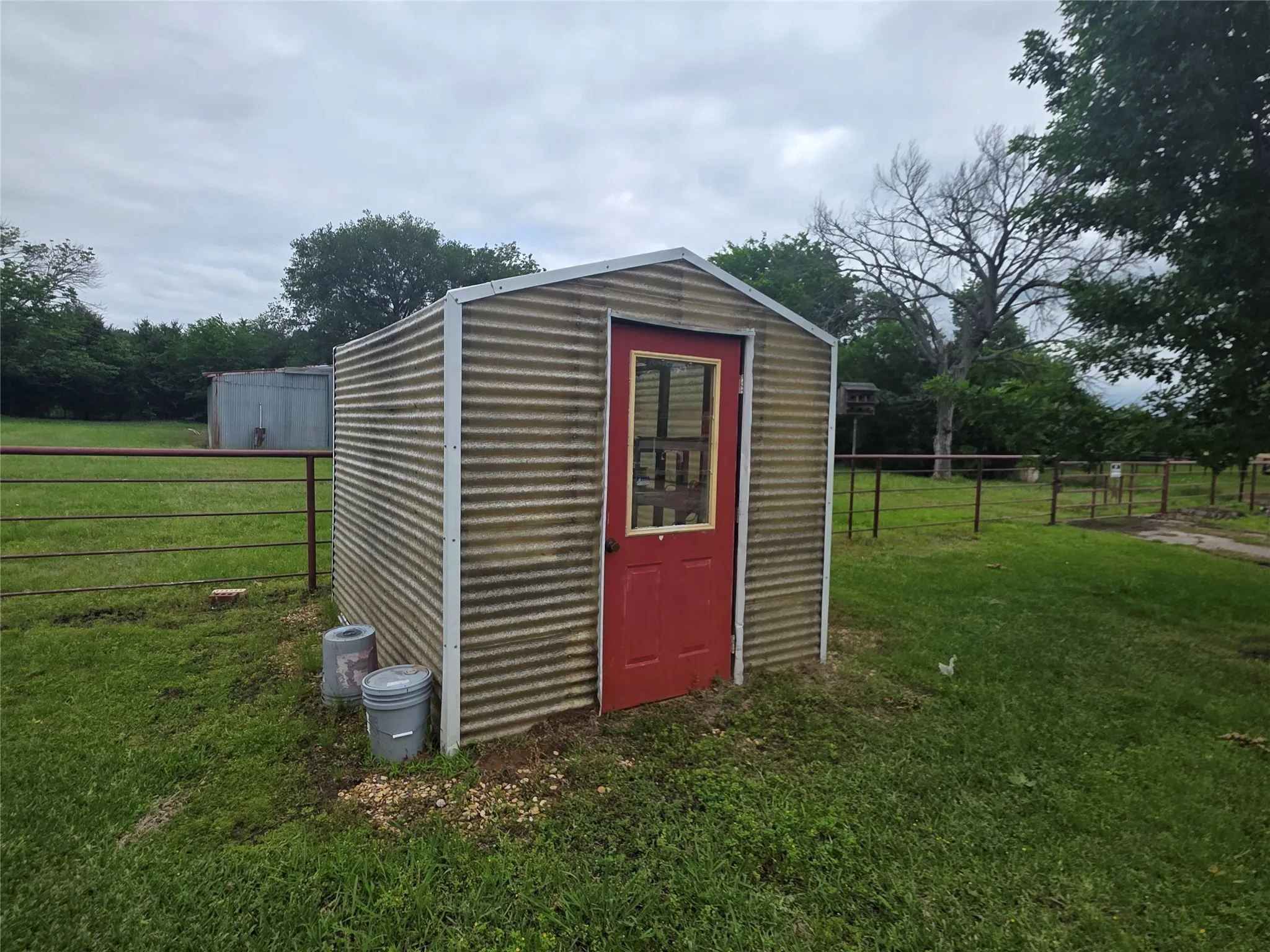 Corrugated metal shed featuring a red entry door with a window panel