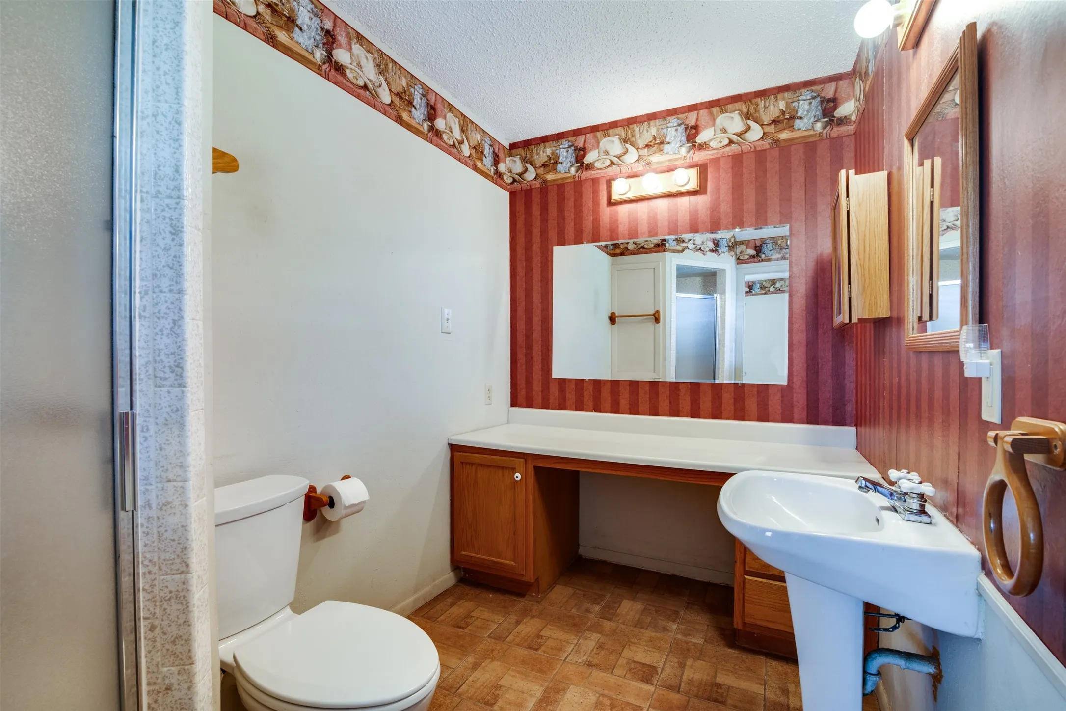 Bathroom featuring a pedestal sink, a wood-finish vanity with a white countertop, a wall-mounted mirror, and a shower enclosure