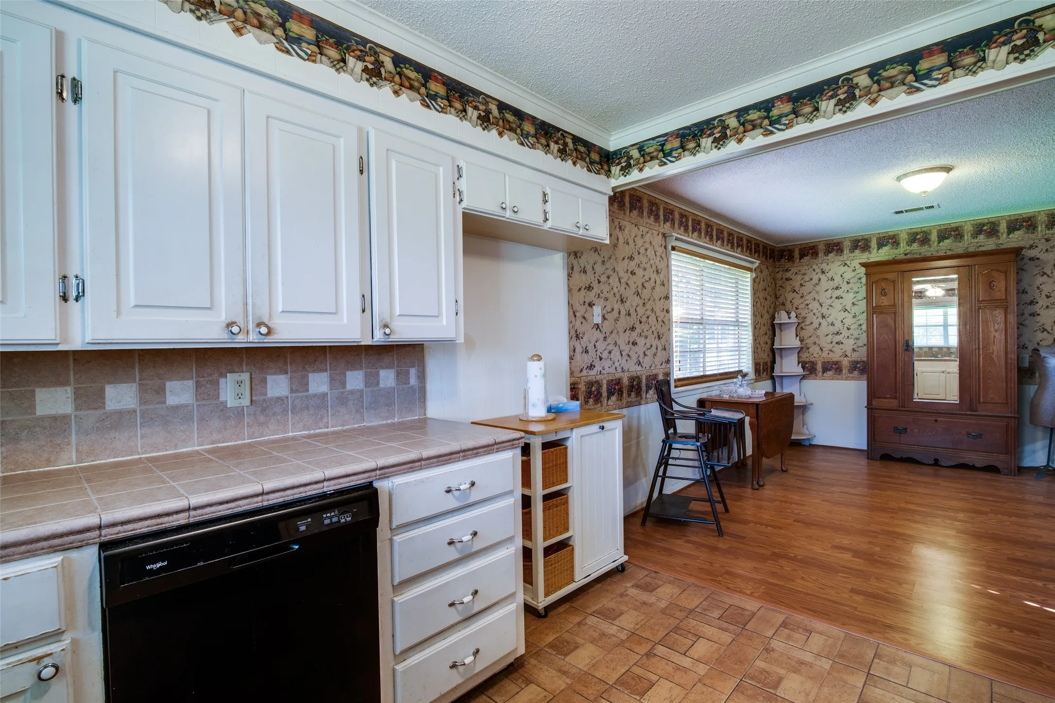 Kitchen area featuring white cabinetry with silver-tone hardware, a tiled countertop, and a black dishwasher