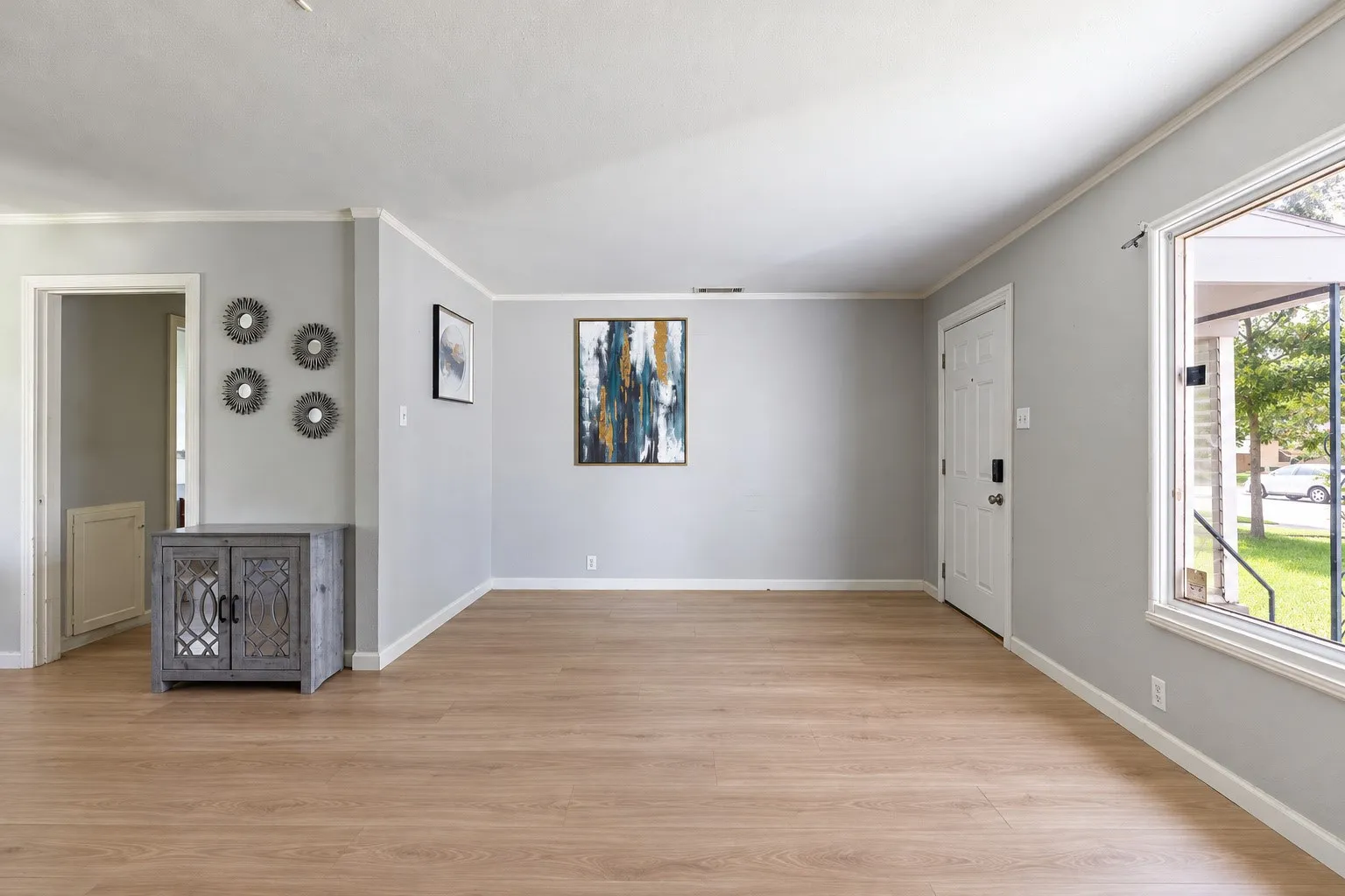 Spacious room featuring wood-finish flooring, light grey painted walls, white trim, and a large window