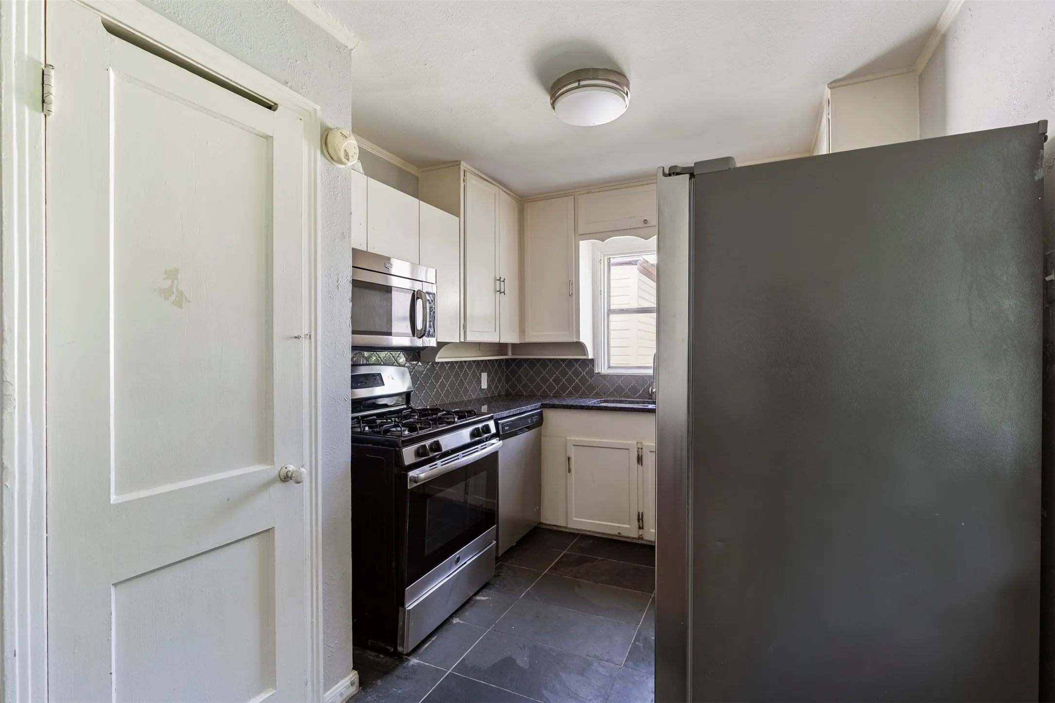 Kitchen featuring white cabinetry, stainless steel appliances, dark countertop, diagonal tile backsplash, and dark tile flooring