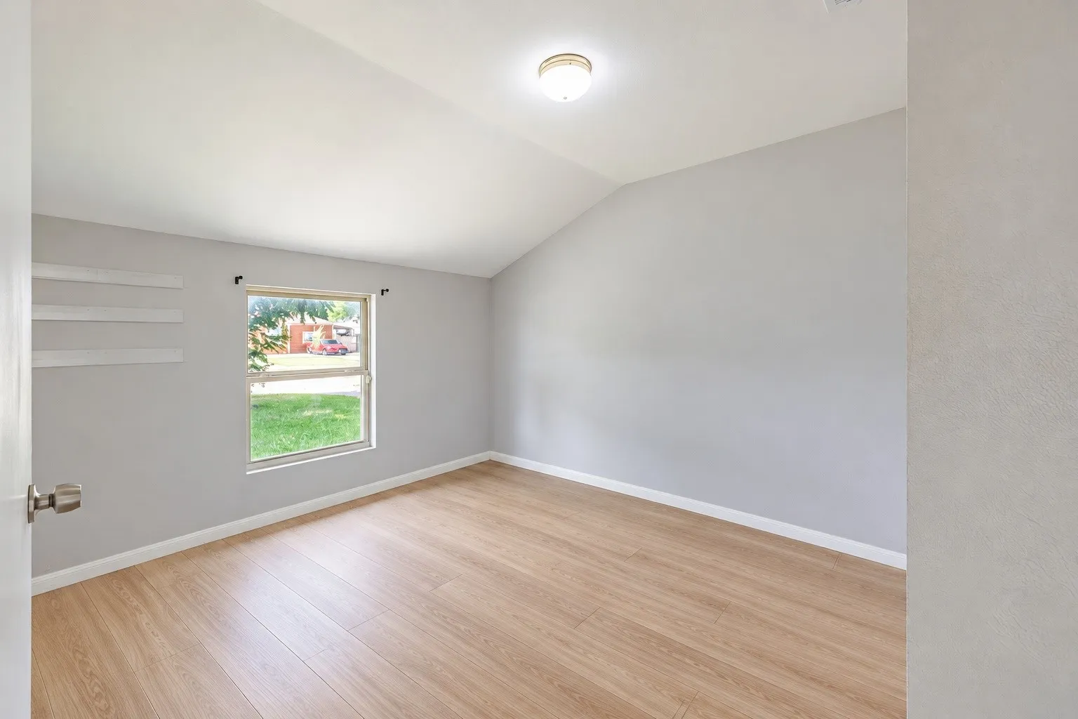 Vaulted ceiling, wood-finish flooring, neutral paint palette, flush-mount lighting, and white baseboards