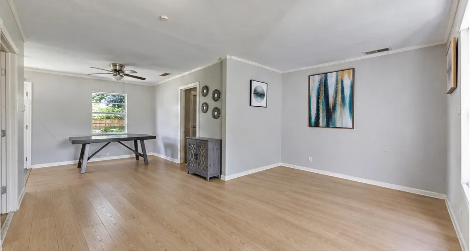 Expansive living area featuring light wood-finish flooring, a ceiling fan with light, and light gray wall finishes