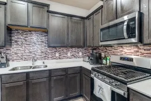 Kitchen featuring a gas range, stainless steel microwave, dual basin sink, white countertops, and wood cabinetry with a tile backsplash