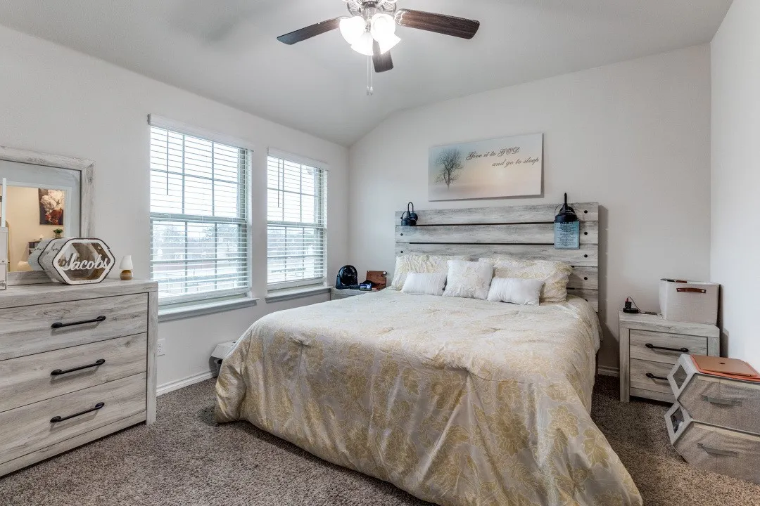 Carpeted bedroom featuring two large windows with blinds, a ceiling fan with integrated lighting, and white walls
