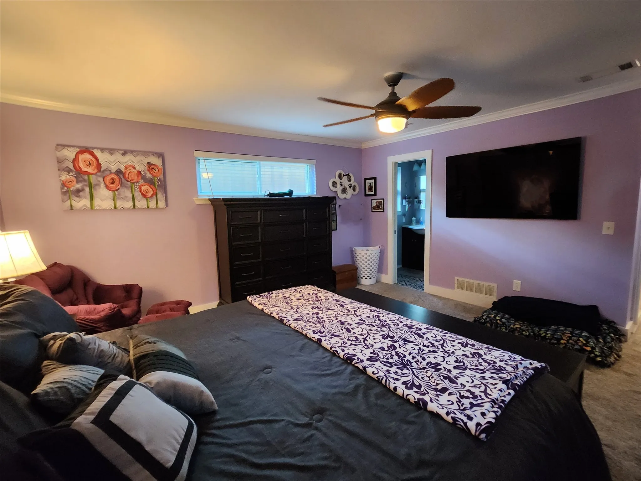 Spacious interior room featuring crown molding, a ceiling fan with integrated lighting, a wall-mounted display, and a doorway leading to an adjoining space with a vanity