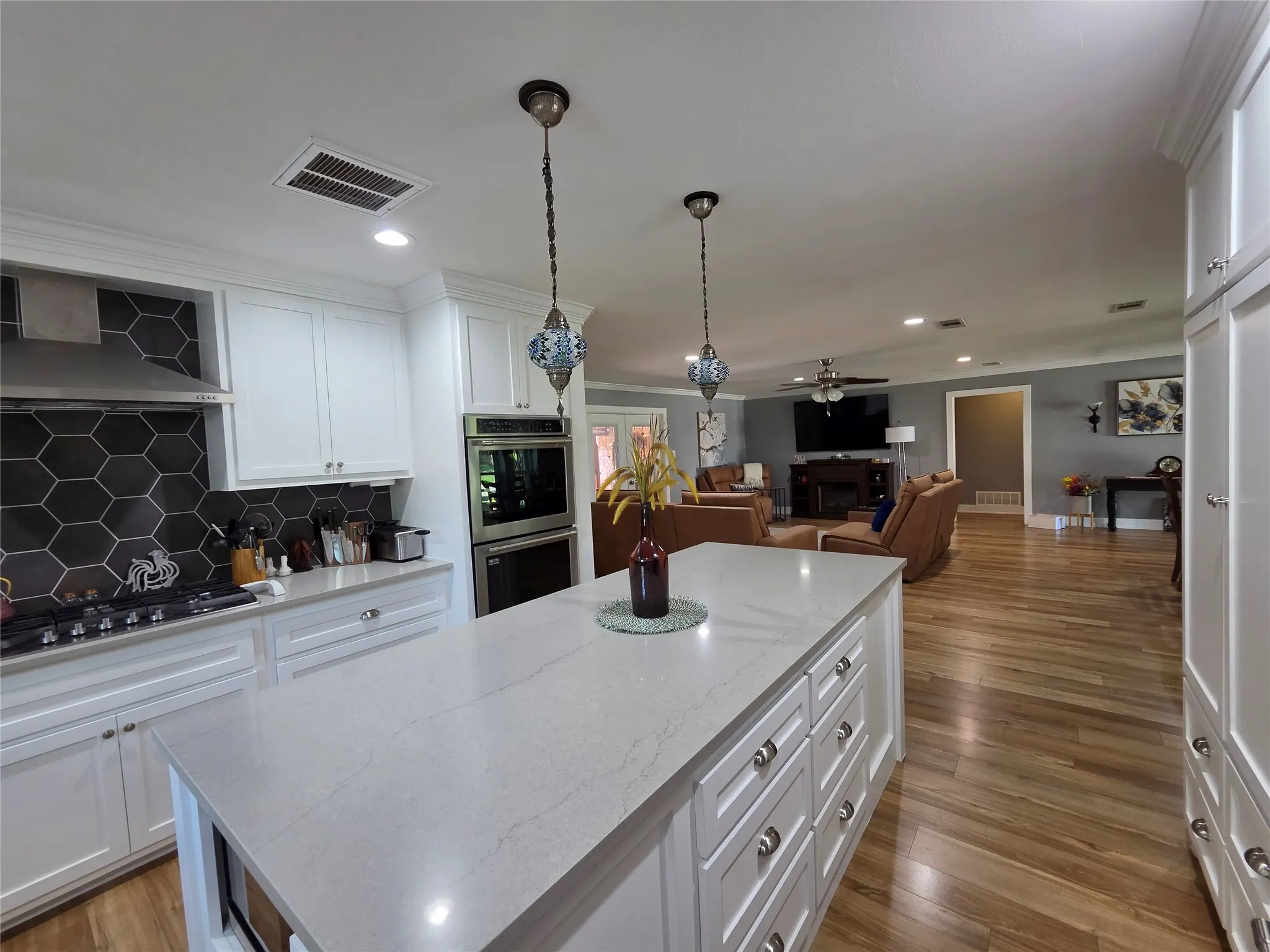 Kitchen featuring a large island with a light-toned countertop, white cabinetry, a hexagonal tile backsplash, and stainless steel double ovens