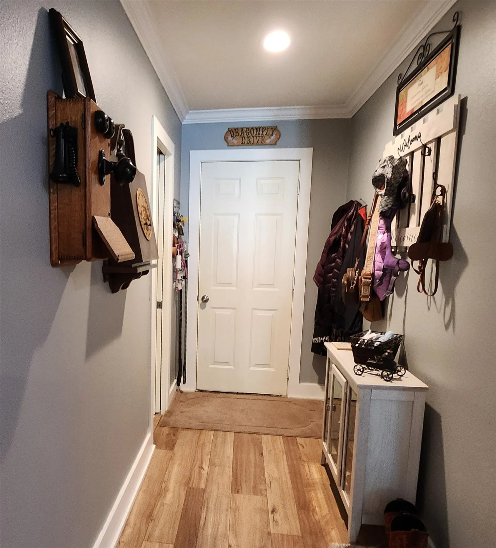 Hallway featuring wood-finish flooring, light gray walls, white baseboards, and crown molding