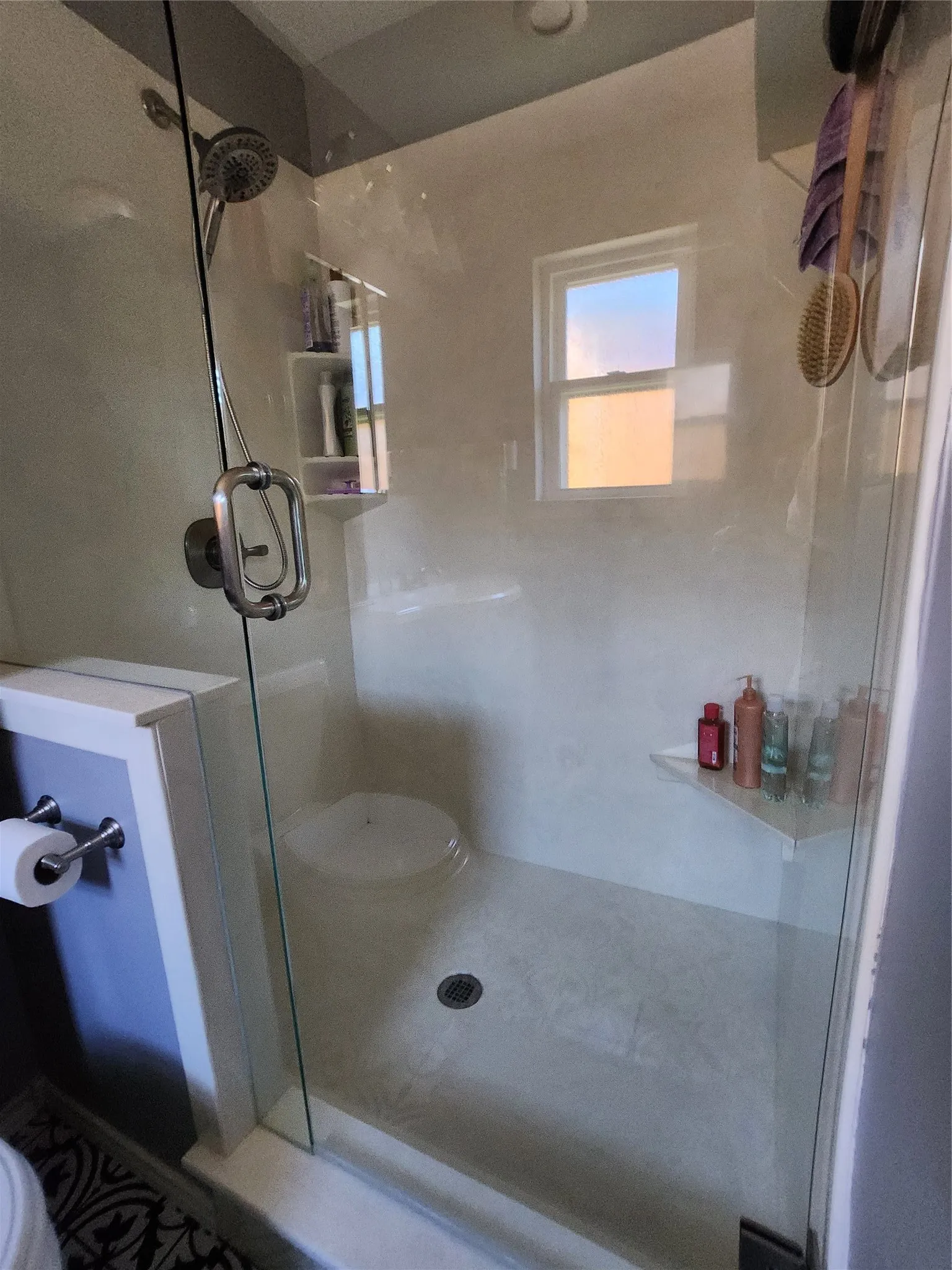 Glass-enclosed shower with a multi-function showerhead, built-in shelving, and a small window for natural illumination