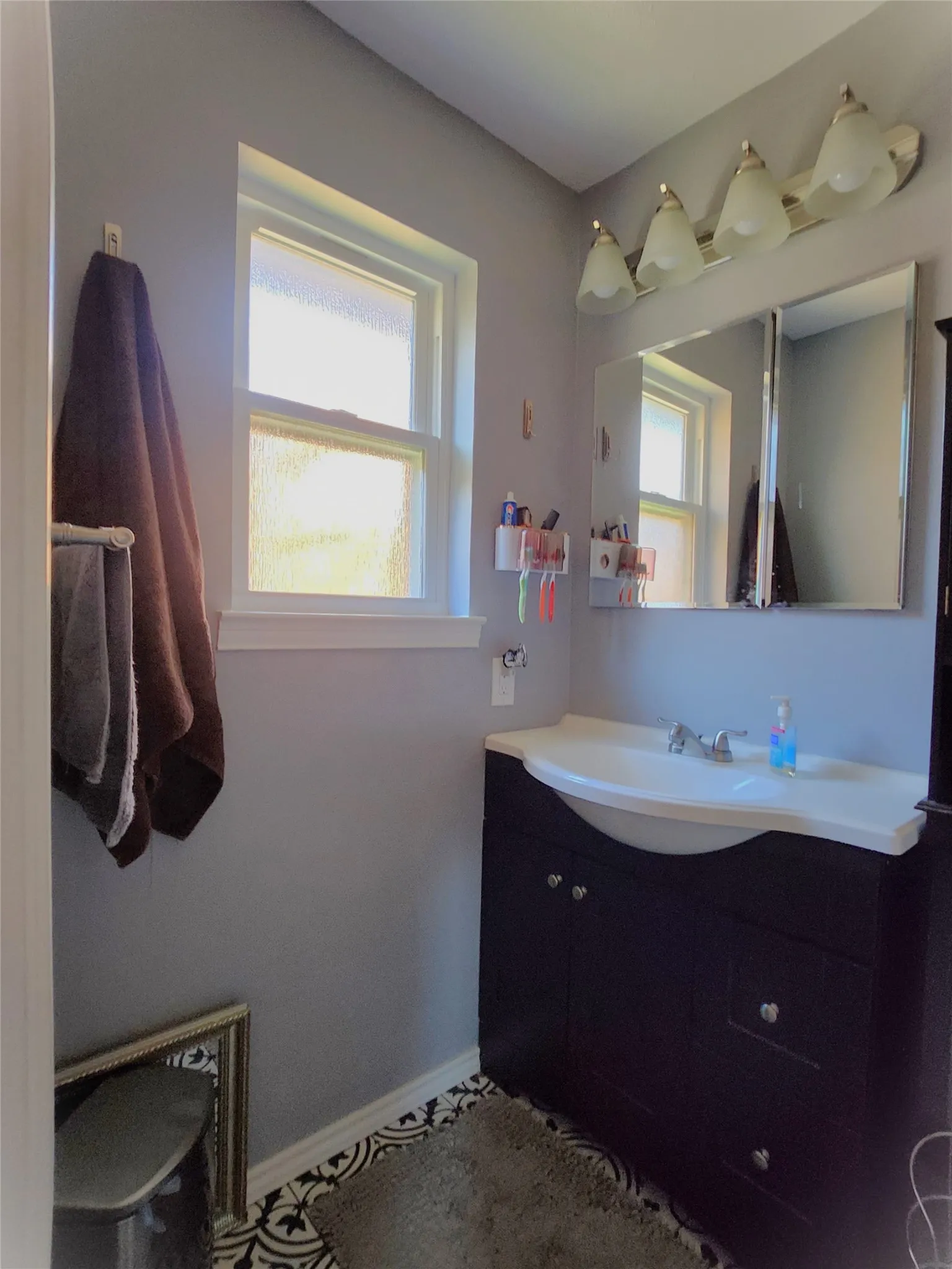 Bathroom featuring a dark wood-finish vanity with an integrated white sink, a vanity mirror, and a four-light fixture