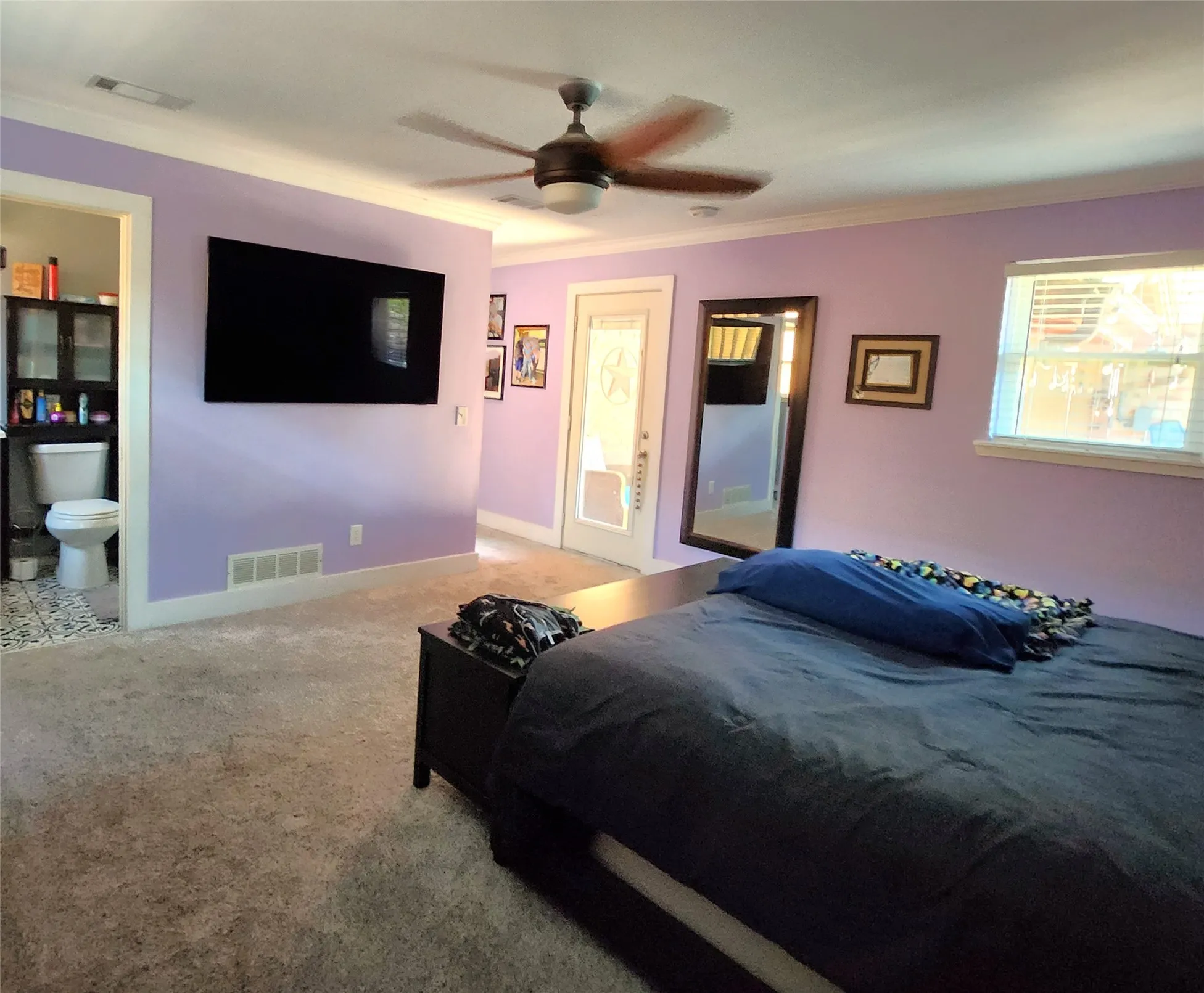 Spacious room featuring light lavender walls, plush carpet flooring, and a ceiling fan