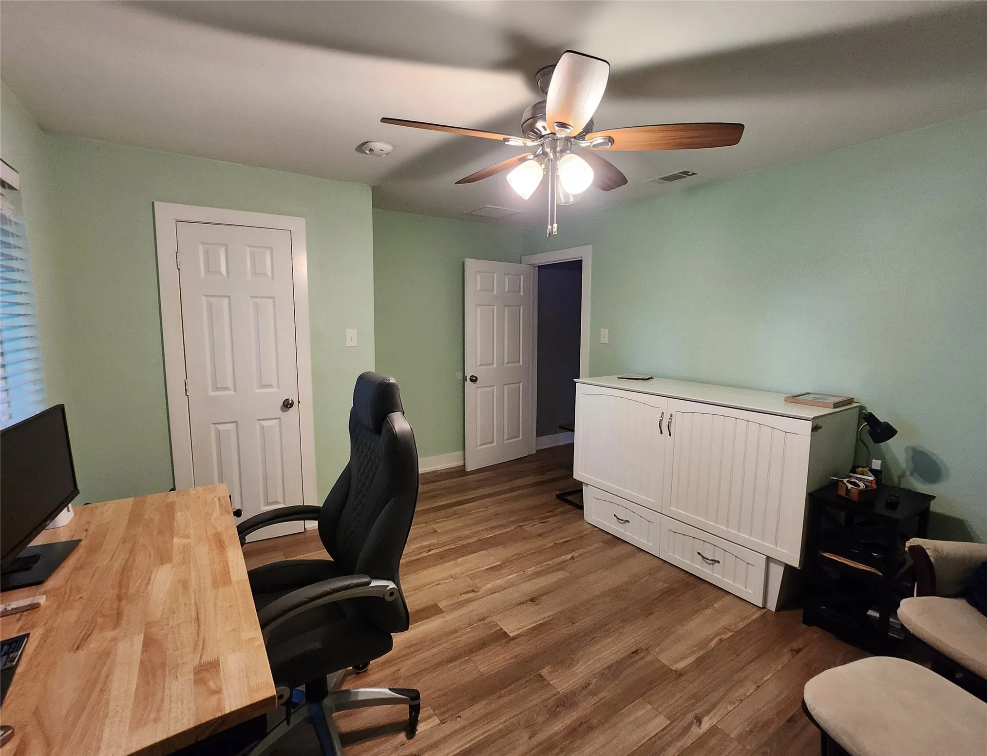Spacious room featuring wood-finish flooring, light green walls, and a ceiling fan with integrated lighting
