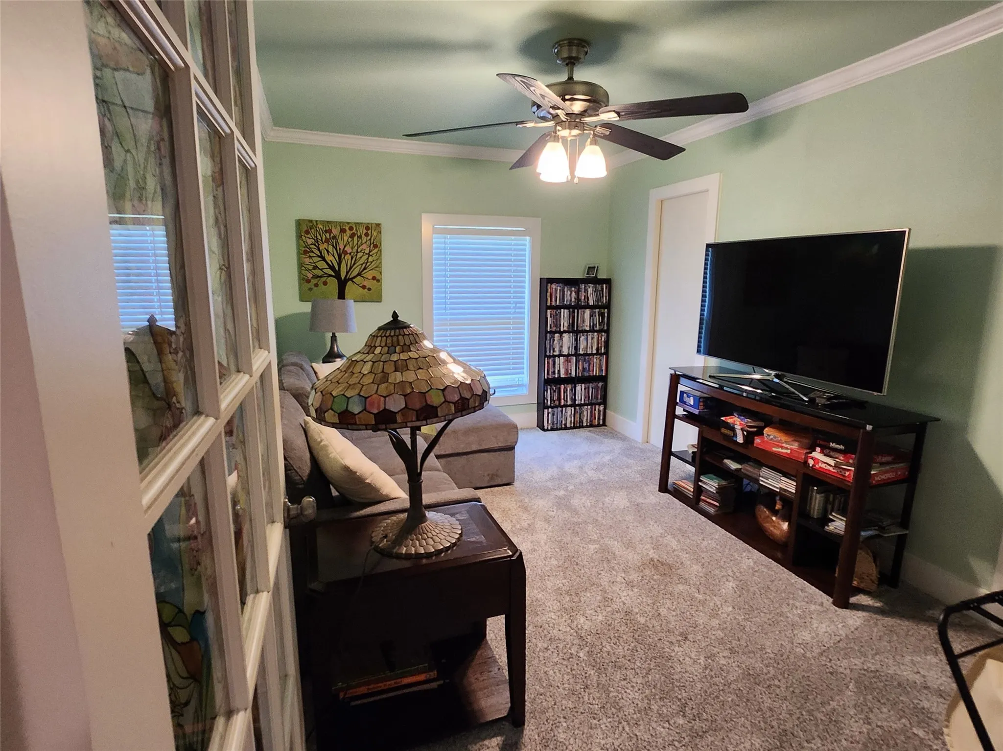 Carpeted living space with crown molding, a ceiling fan with integrated lighting, a window with blinds, and white interior doors