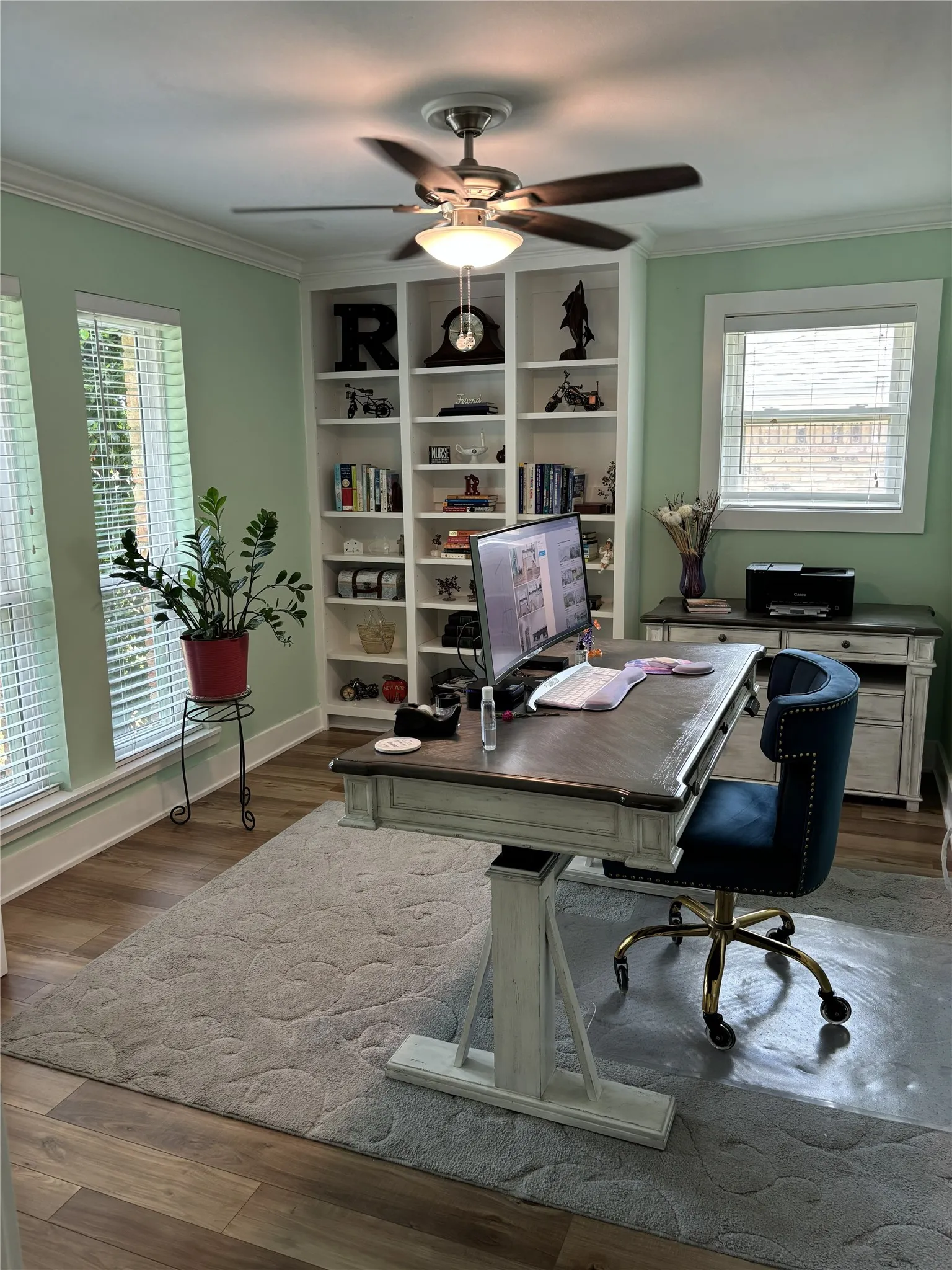 Room currently used  as Home Office, wood-finish flooring, a ceiling fan with integrated lighting, and built-in shelving
