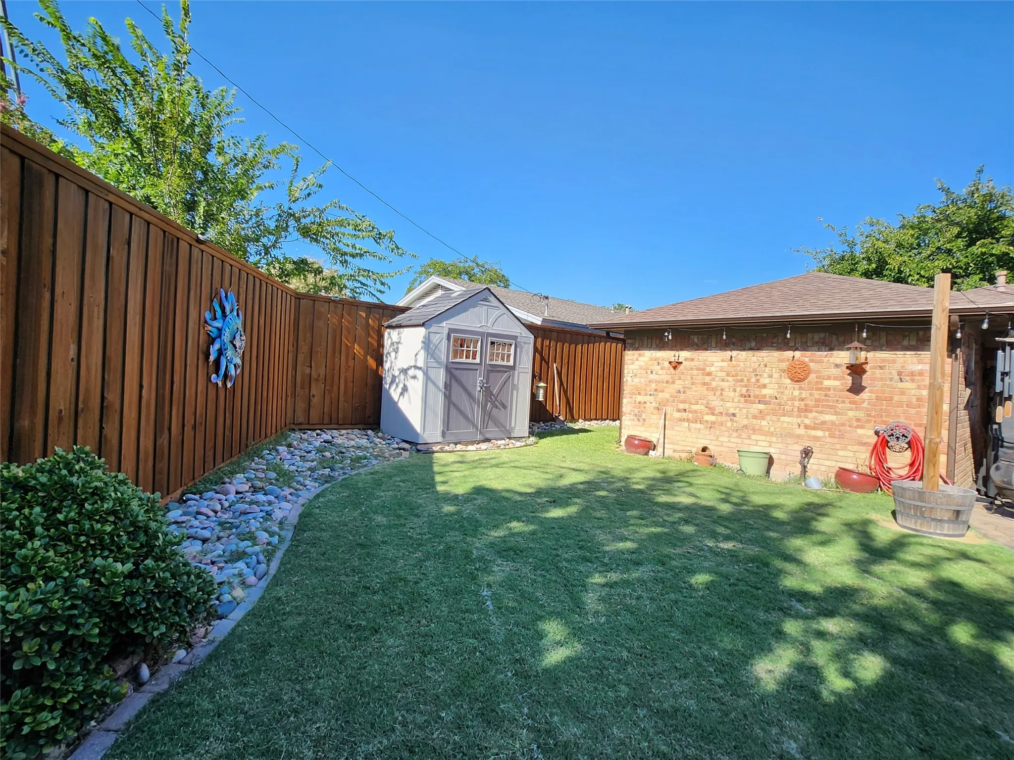 Manicured lawn with a privacy fence, brick exterior, and a detached storage shed