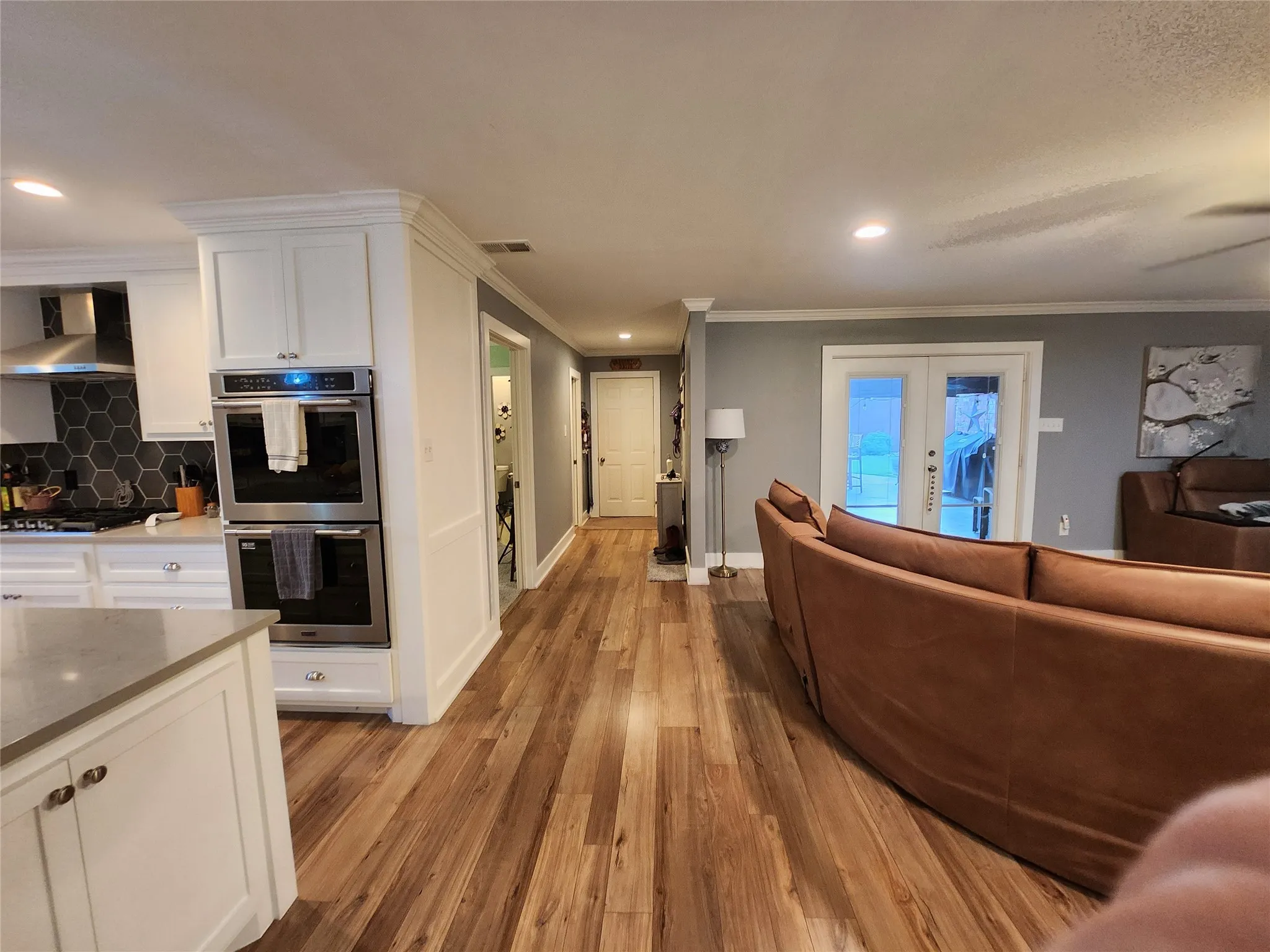 Open-concept kitchen and living area featuring wood-finish flooring, recessed lighting, and crown molding