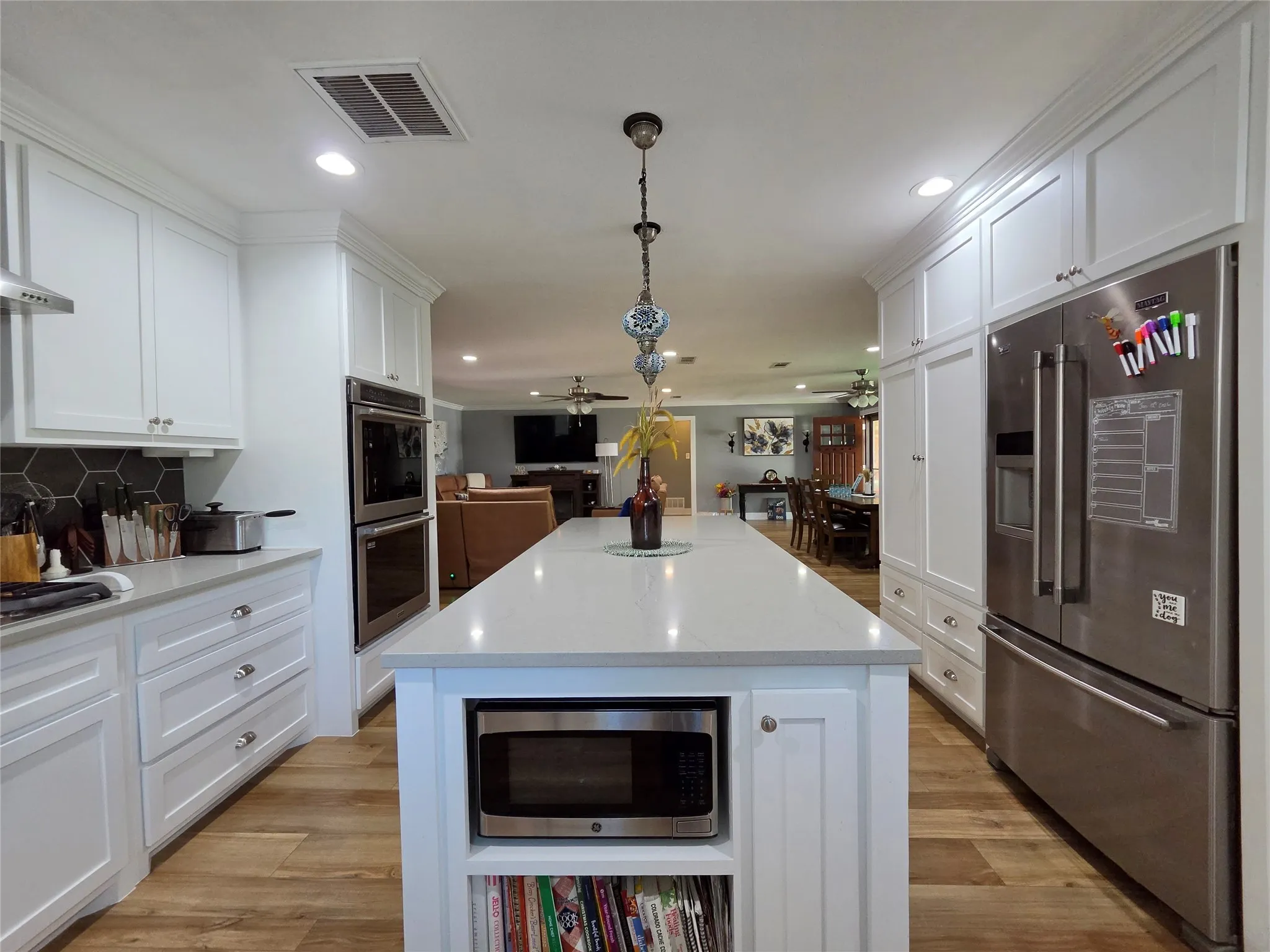 Expansive kitchen island with a light-toned countertop, white cabinetry with crown molding, stainless steel appliances, and wood-finish flooring