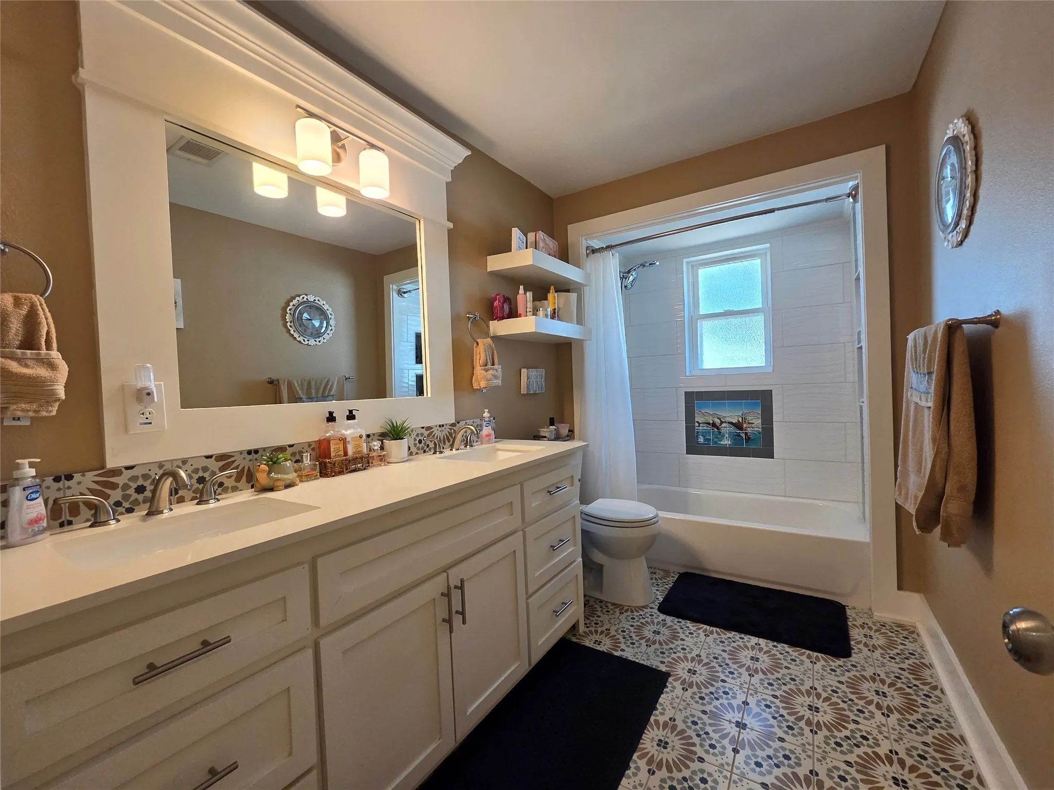Dual vanity with integrated sinks, patterned tile flooring, built-in shelving, full-width mirror, and a tiled shower-tub combination