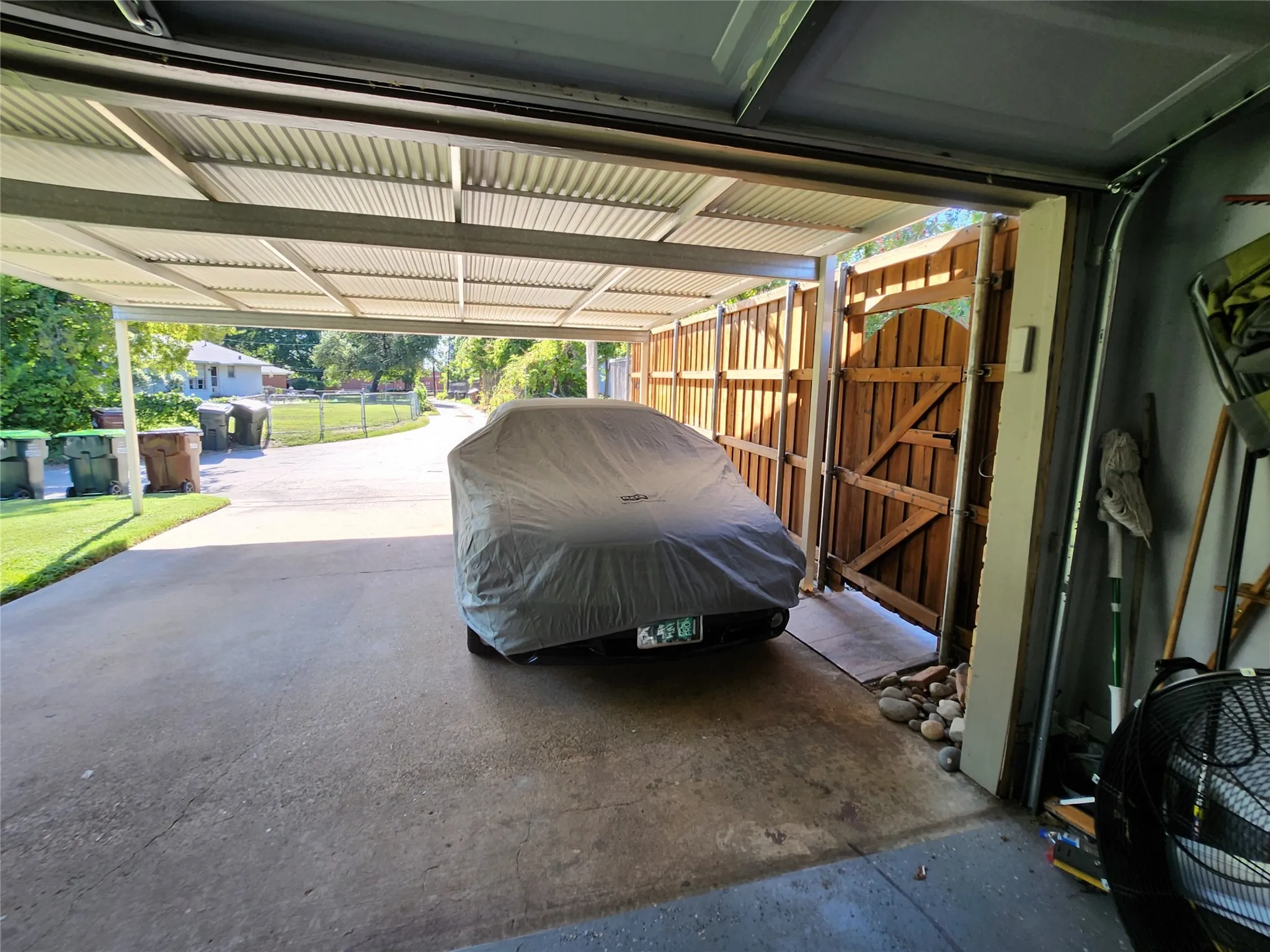 Attached carport and garage entry featuring a concrete driveway, corrugated metal carport roof, and a wooden privacy fence with an arch-top gate