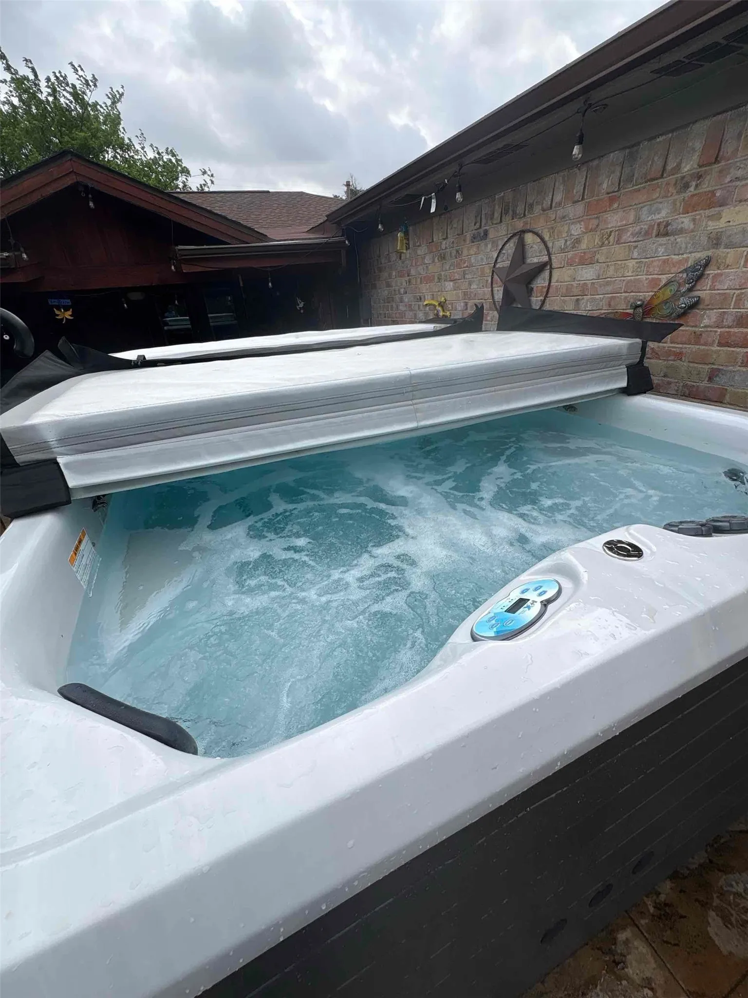 Outdoor hot tub with an integrated control panel, partially covered, set against a brick exterior