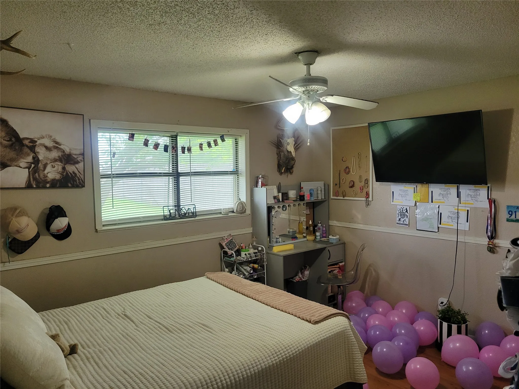 Room featuring wood-finish flooring, a ceiling fan with integrated lighting, and a large window with blinds