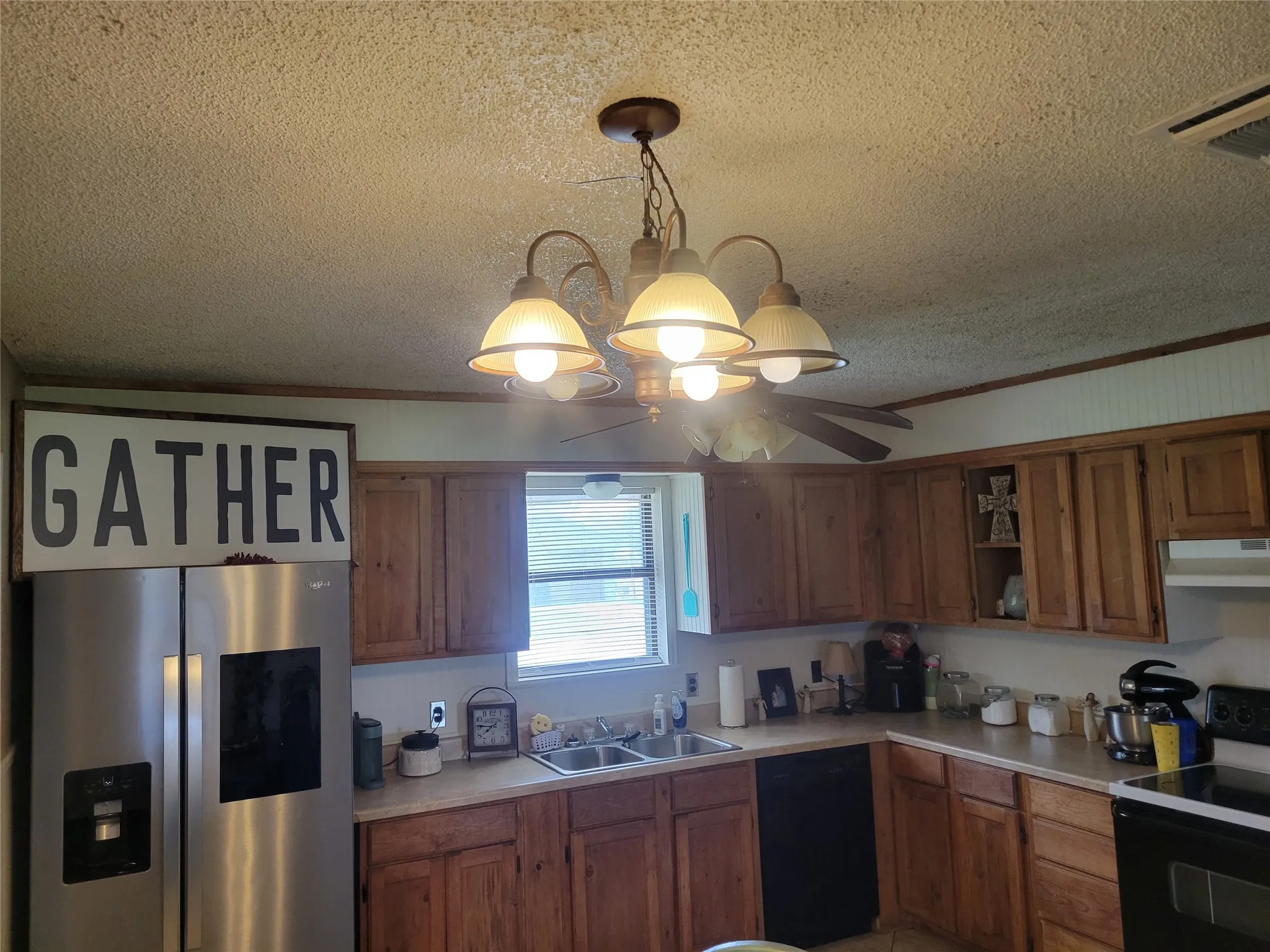 Kitchen featuring wood-finish cabinetry, a stainless steel sink, and a multi-light chandelier