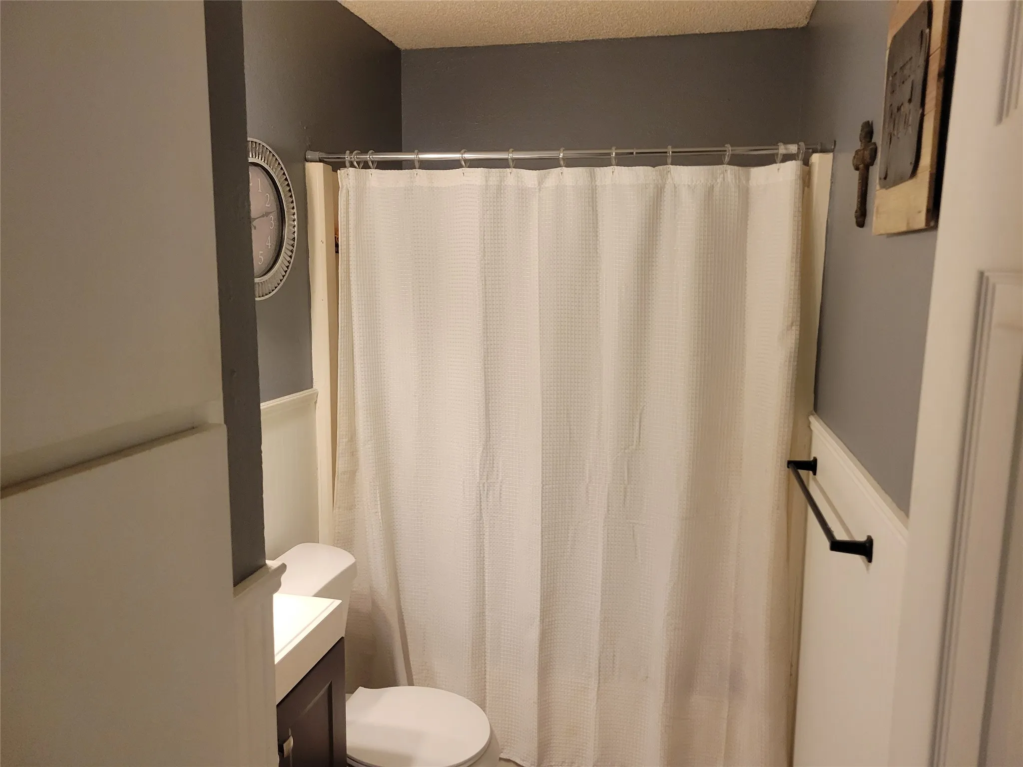 Bathroom featuring a shower/tub combination with a chrome curtain rod, white shower curtain, white wainscoting, and a white toilet