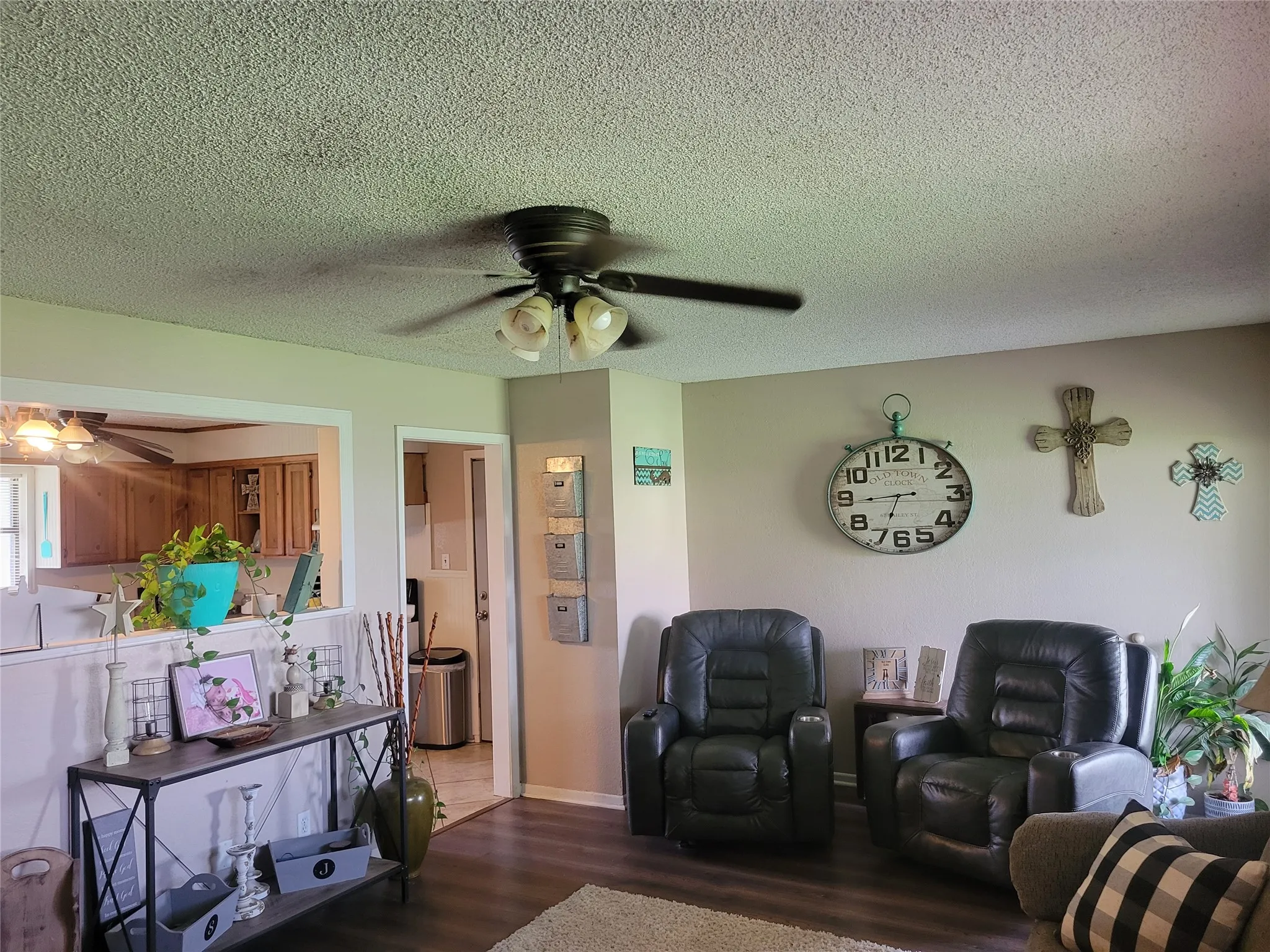 Living area featuring wood-finish flooring, a ceiling fan with integrated lighting, and a pass-through window to the kitchen