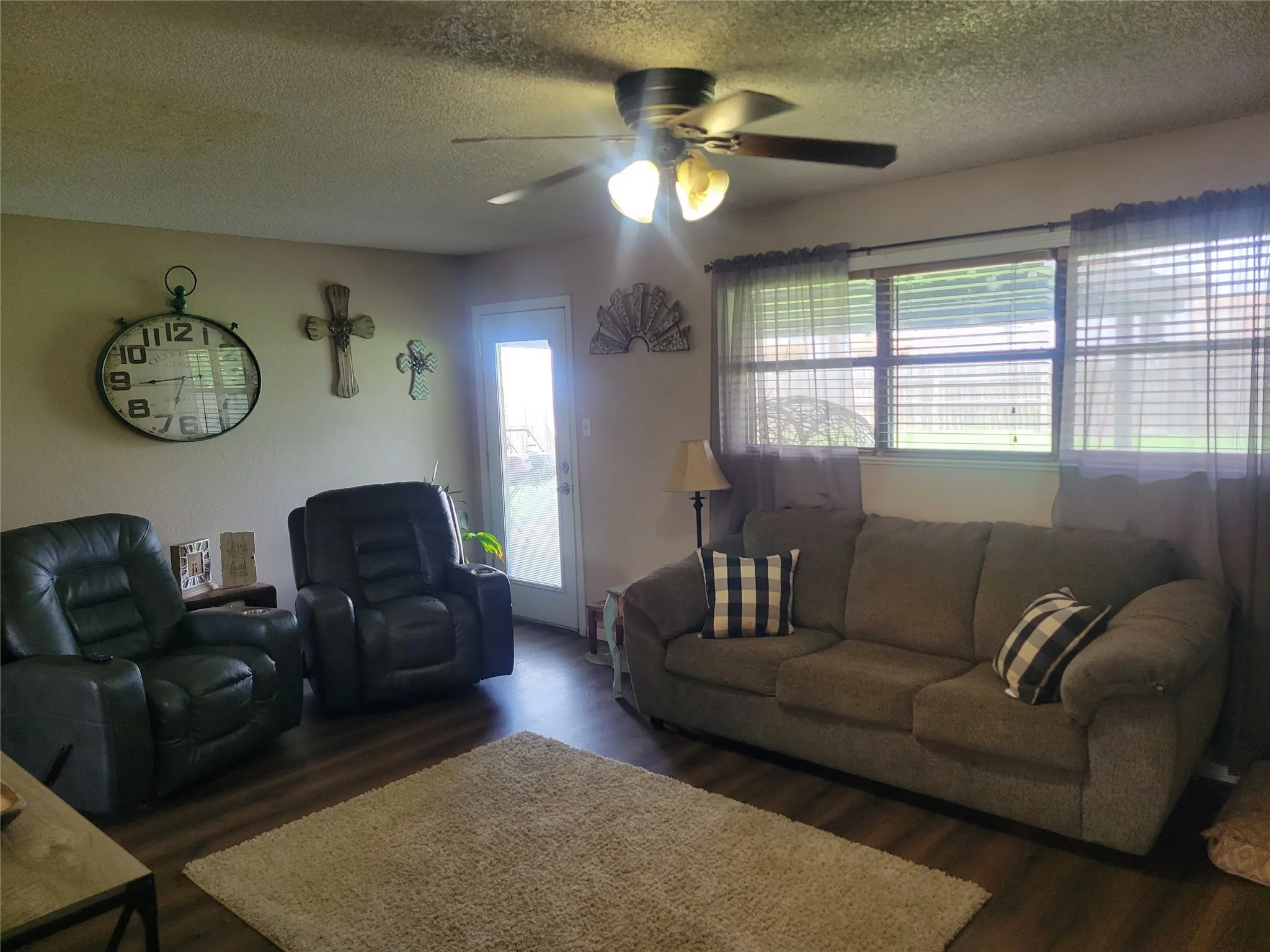 Living area featuring wood-finish flooring, a ceiling fan with integrated lighting, and multiple windows with blinds
