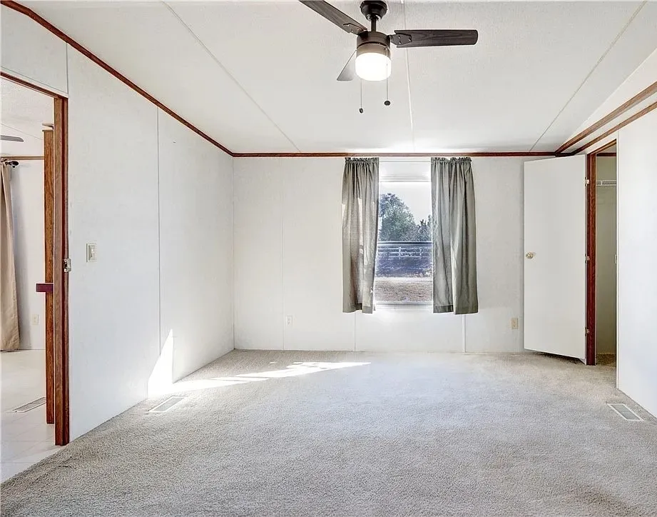 Carpeted interior space featuring white walls with wood trim accents and a ceiling fan