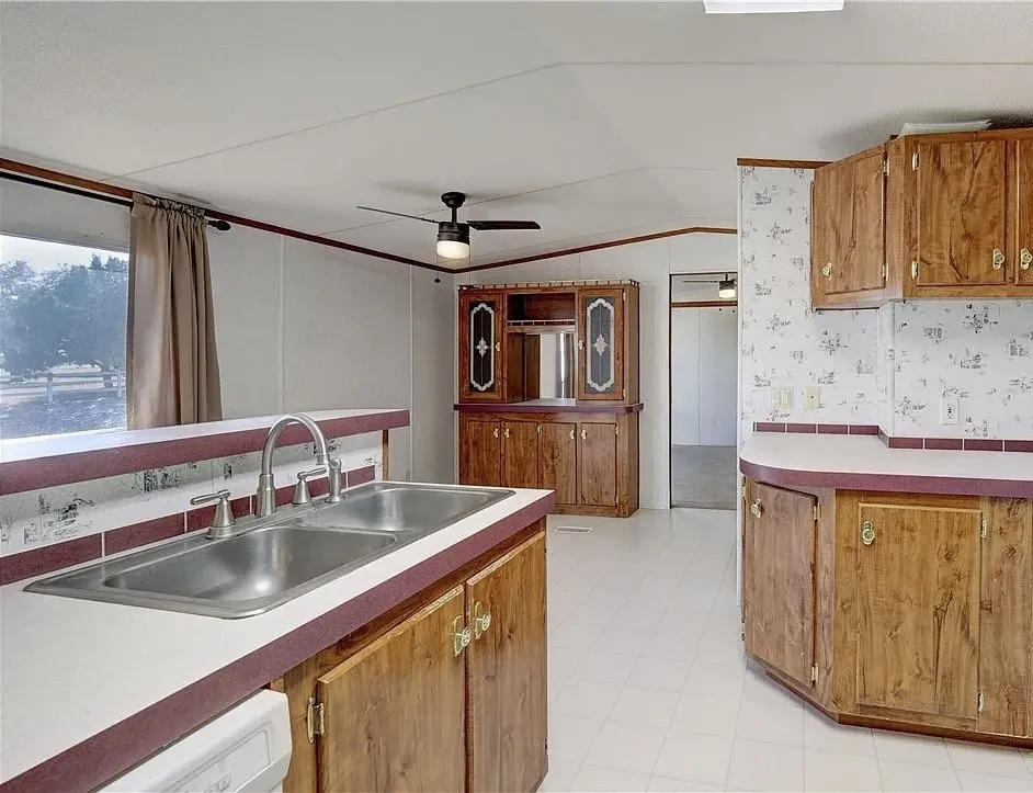 Kitchen featuring wood-finish cabinetry, a double basin stainless steel sink, and white countertops with a contrasting trim