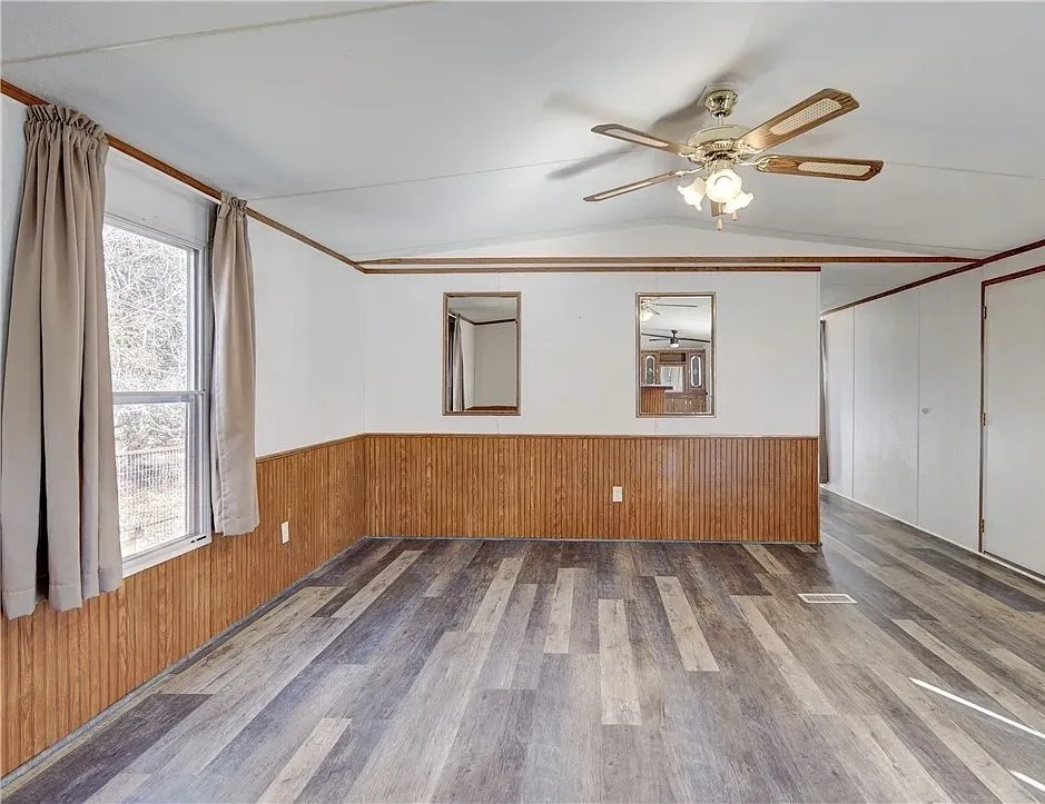 Spacious room featuring wood-finish flooring, half-wall wood paneling, and a ceiling fan