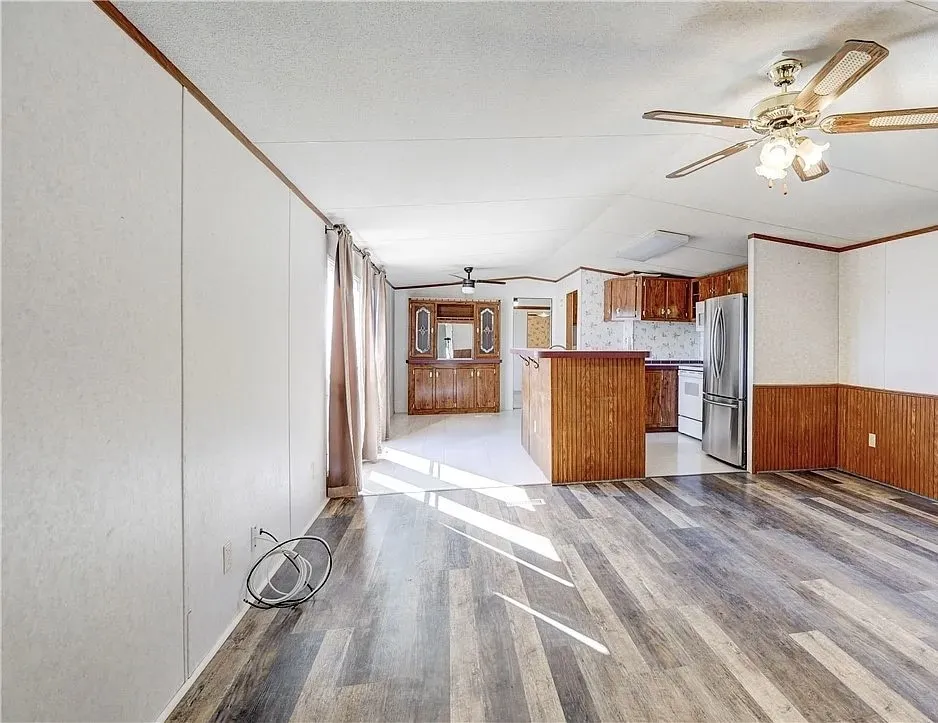 Open-concept living space featuring wood-finish flooring, a ceiling fan with integrated lighting, and white paneled walls with wood trim