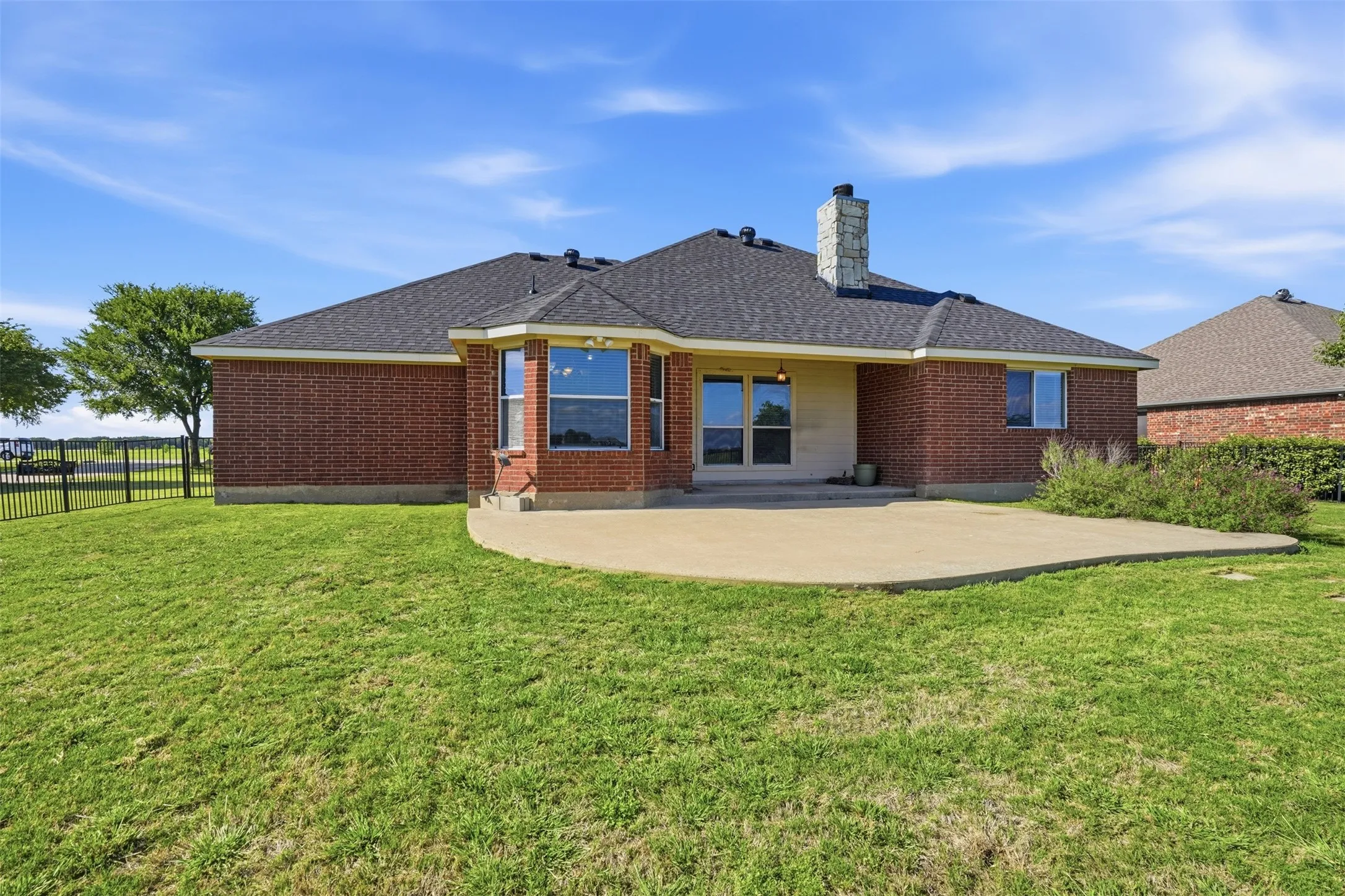Expansive back yard featuring a large concrete patio, covered porch and iron fencing.